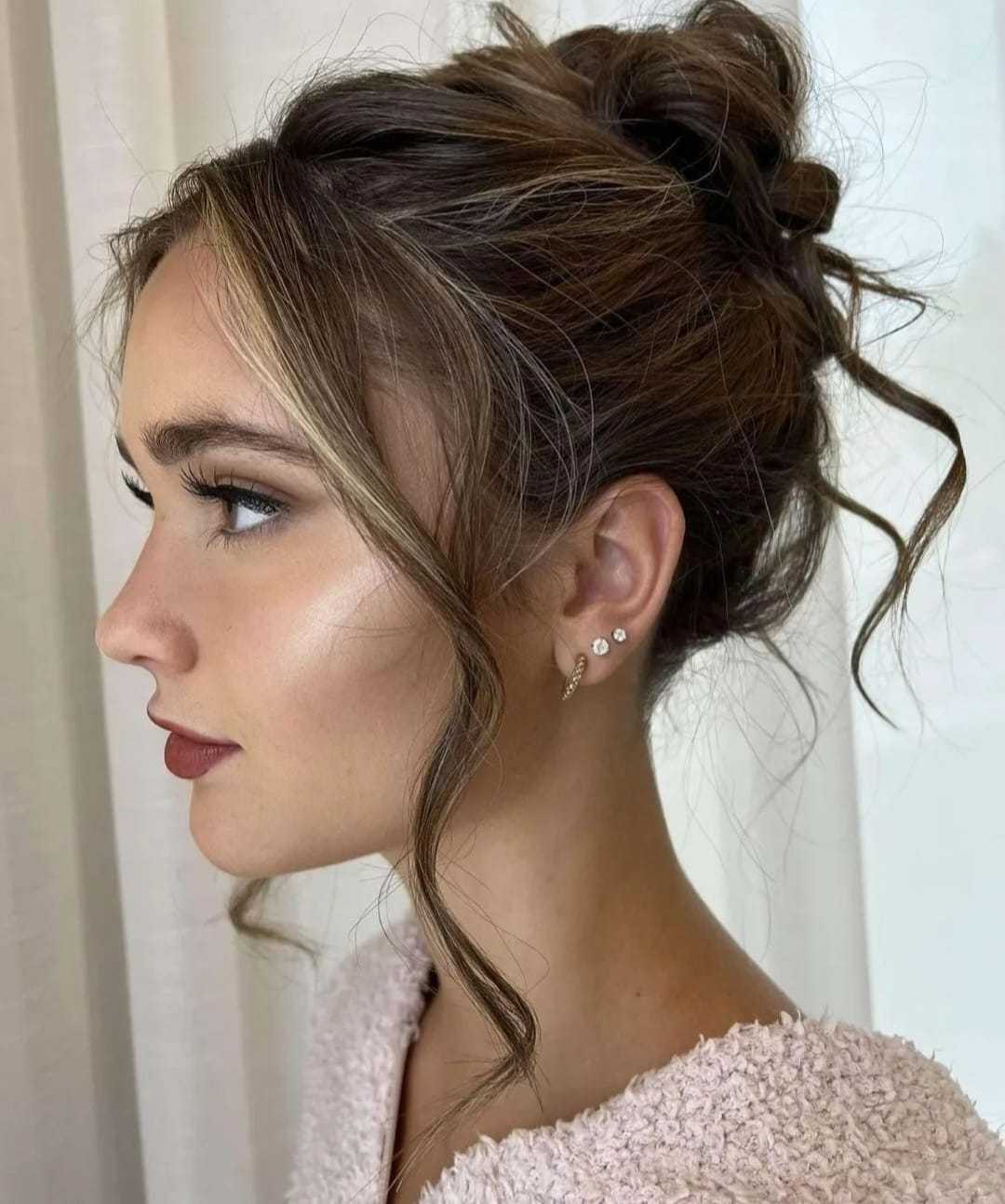 Woman with elegant updo hairstyle and earrings, looking sideways.