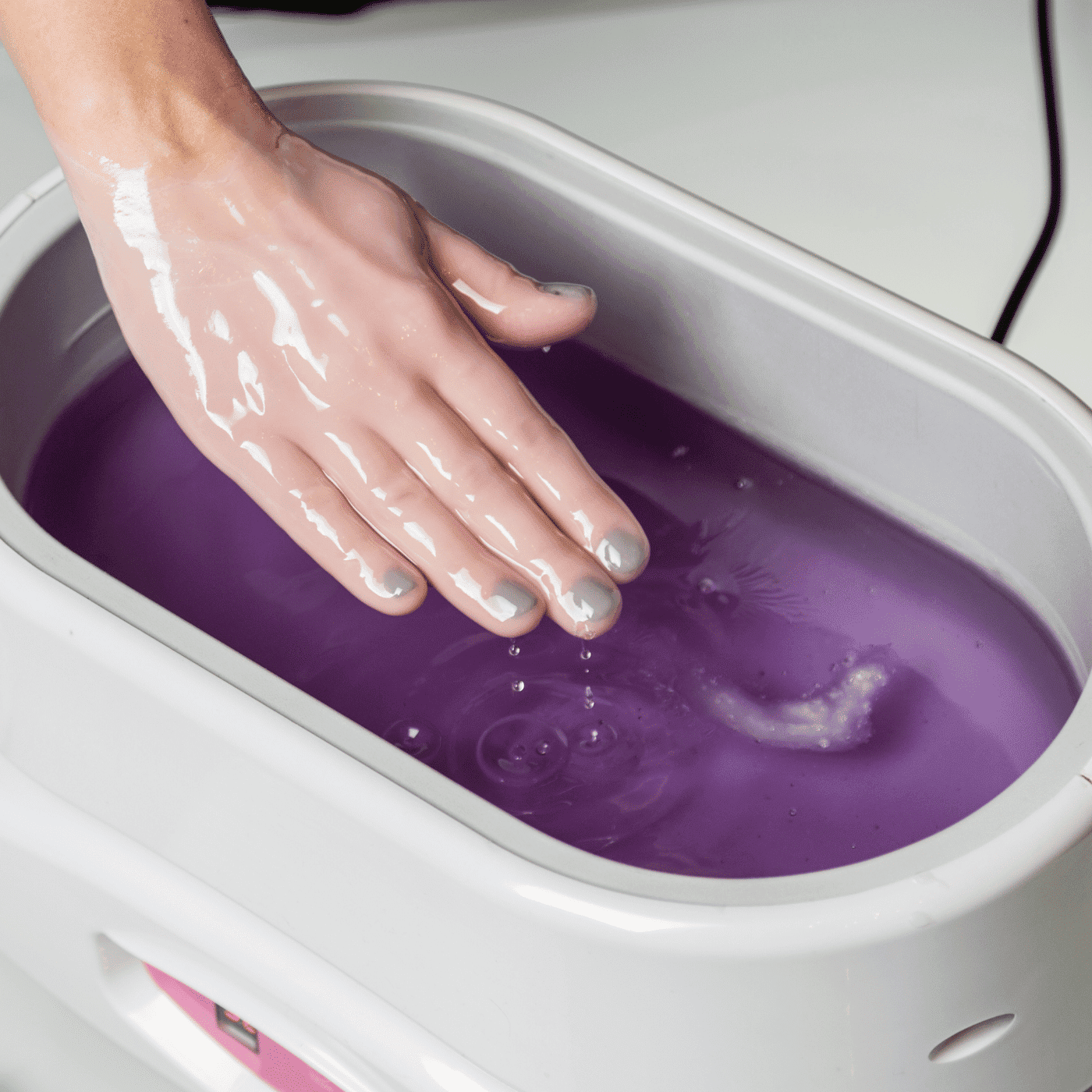 Hand dipping into purple paraffin wax bath for spa treatment.