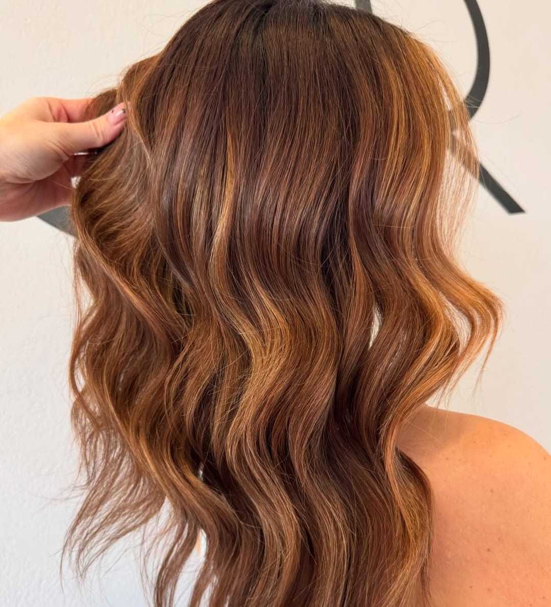 Wavy light brown hair with highlights being styled by a hand.