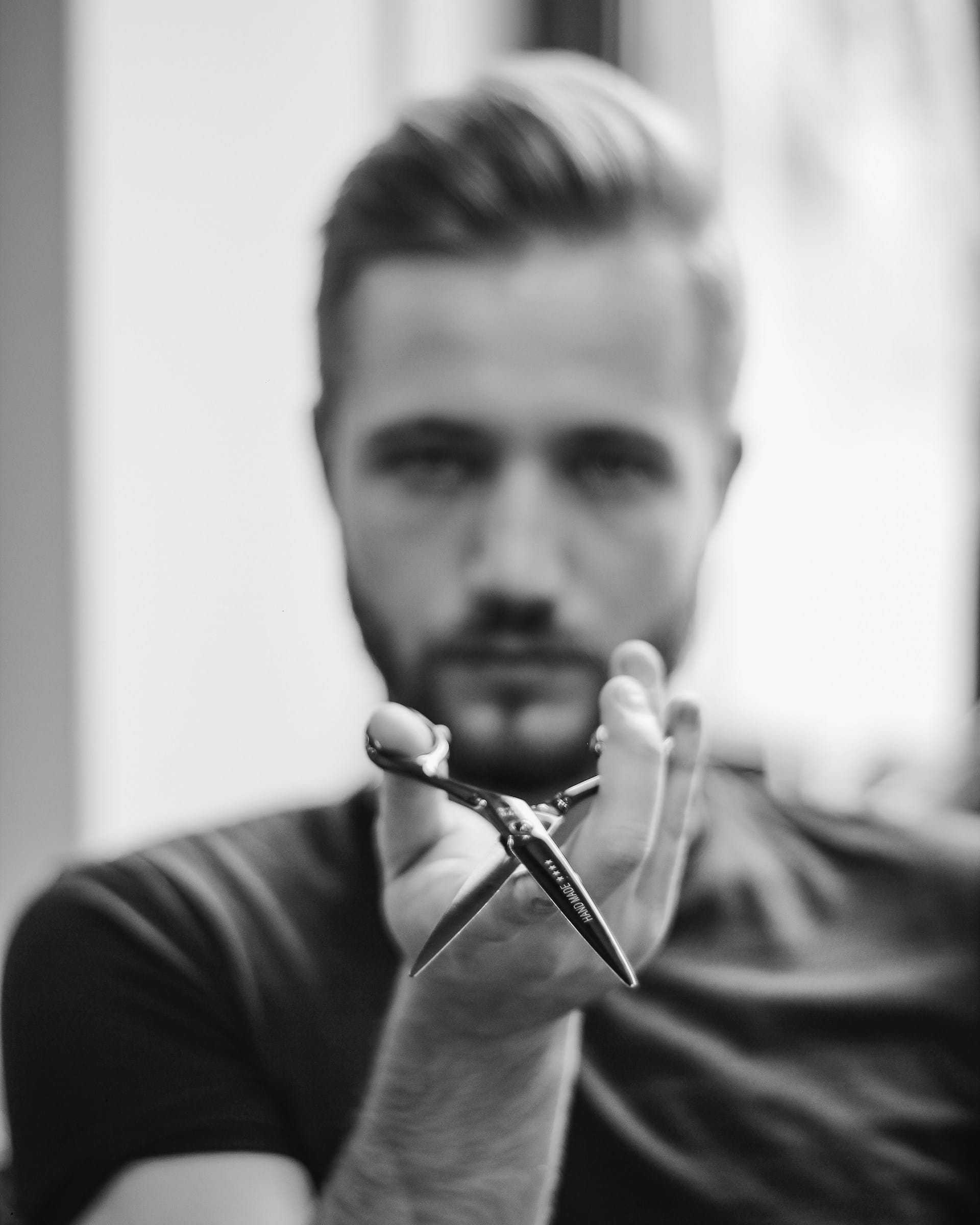 Man holding scissors in focus, black and white photo.