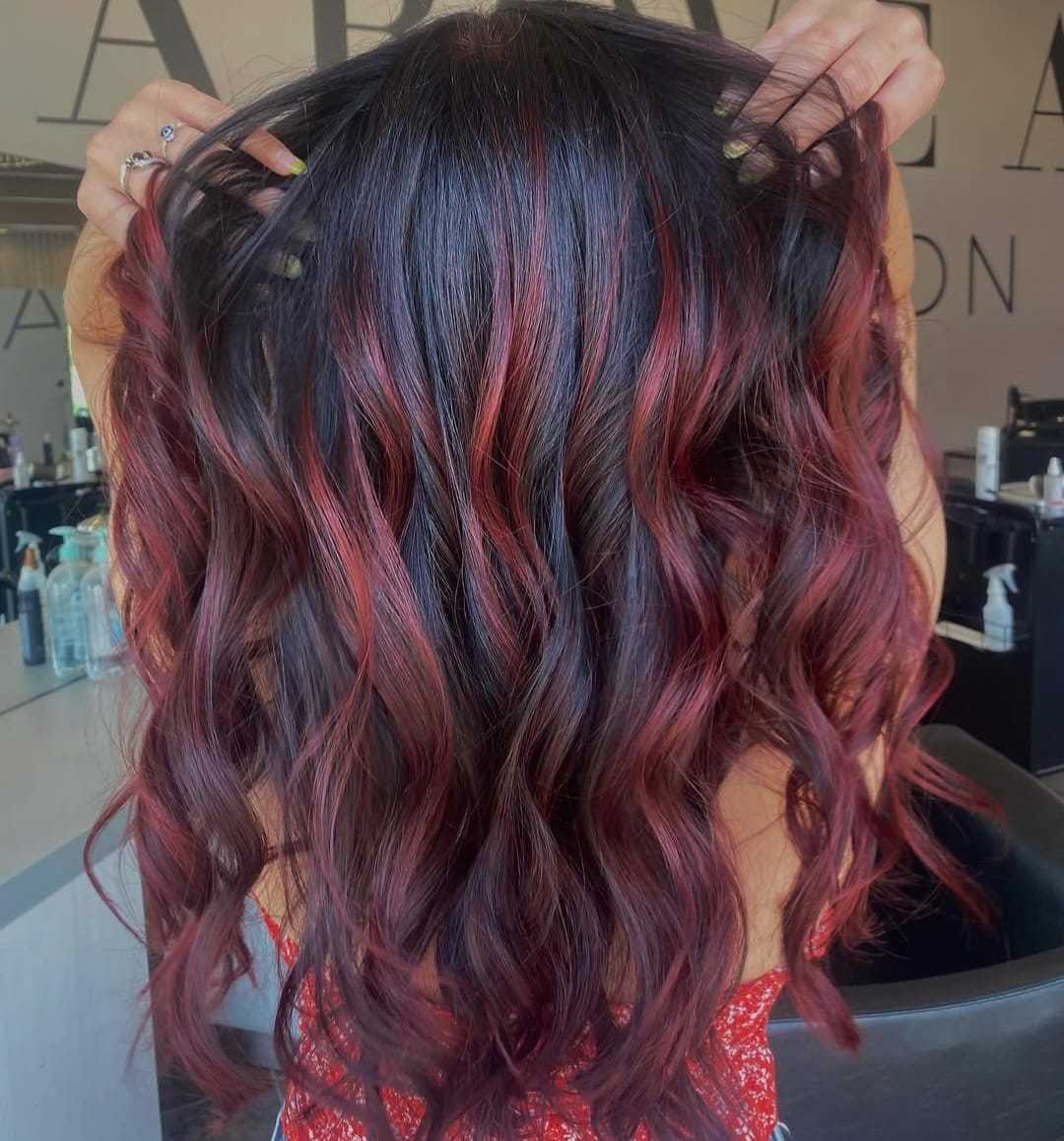 Wavy dark hair with vibrant red highlights in a salon setting.