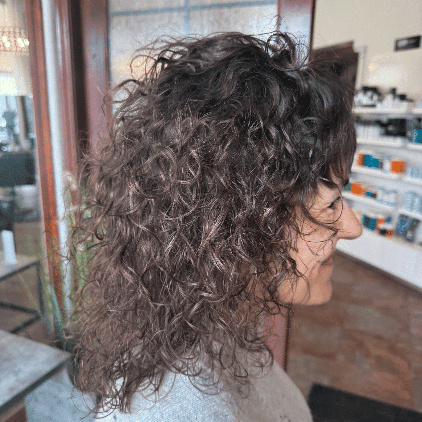 Curly-haired person at a salon, side profile view.