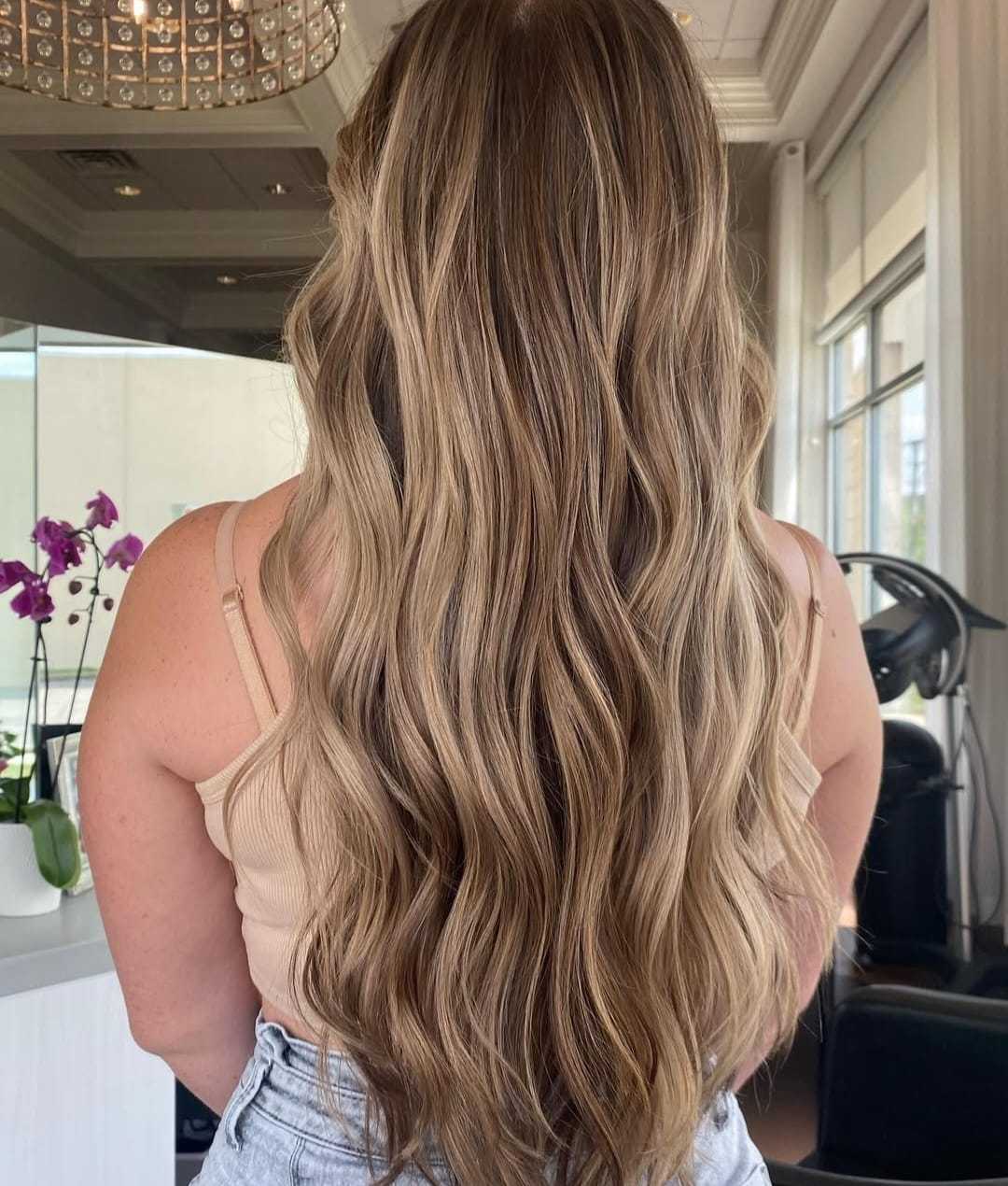 Long, wavy, blonde hair styled in soft curls, viewed from behind in a salon setting.