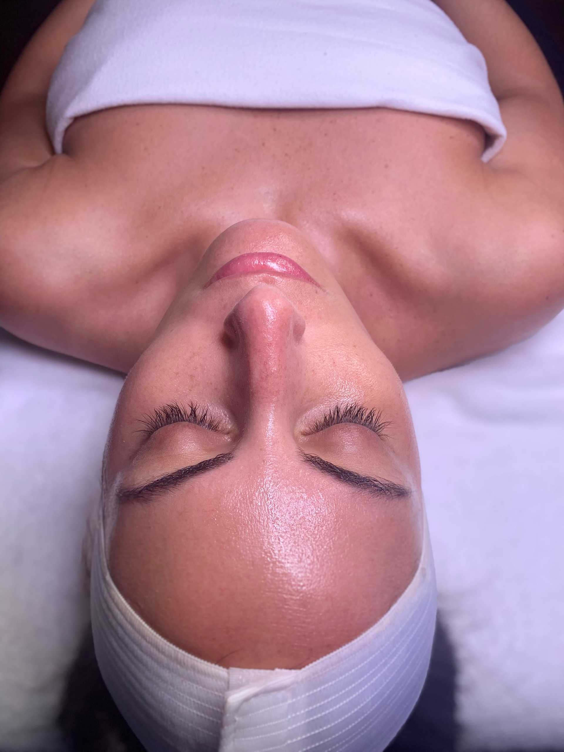 Person lying supine with closed eyes, headband, and glowing skin, suggesting relaxation.