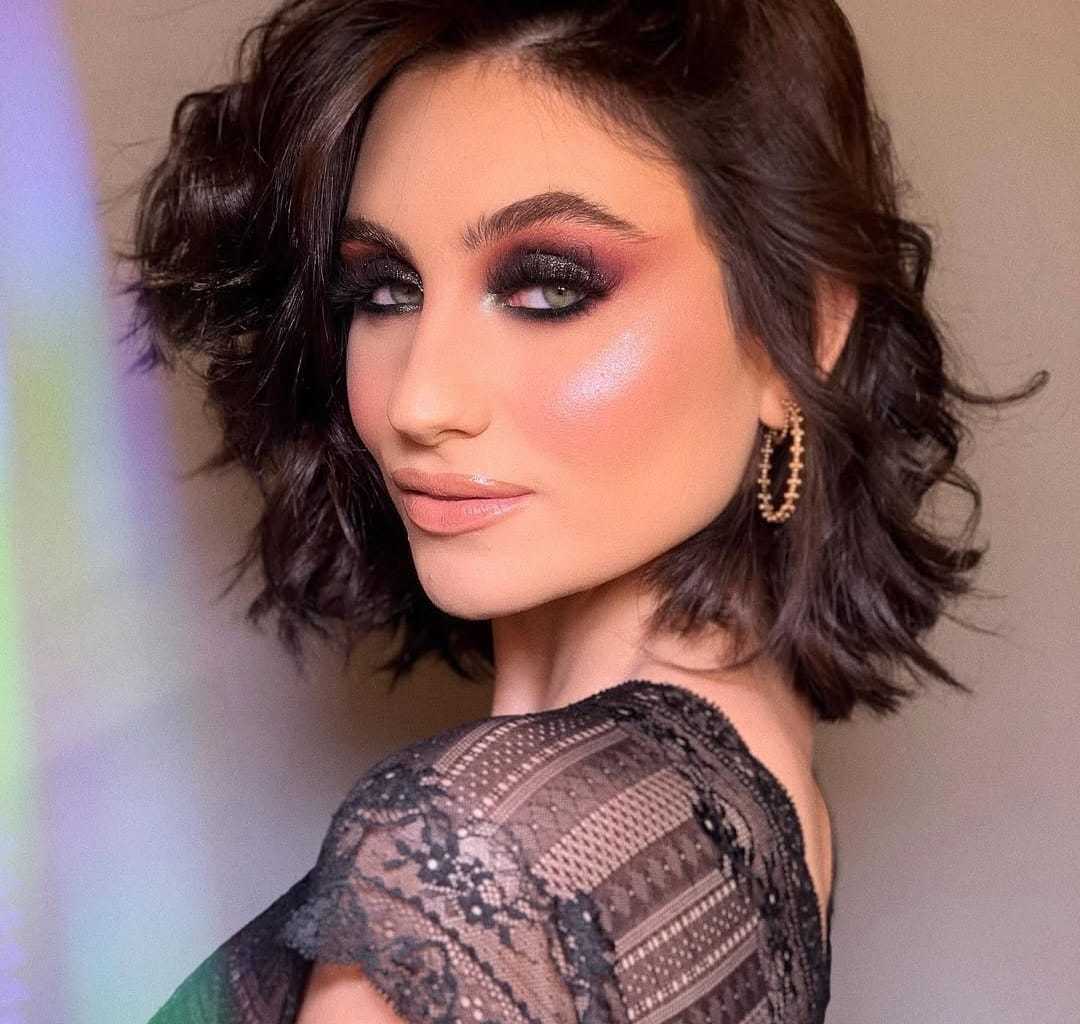 Brunette with smokey eye makeup, glossy lips, and lace top.