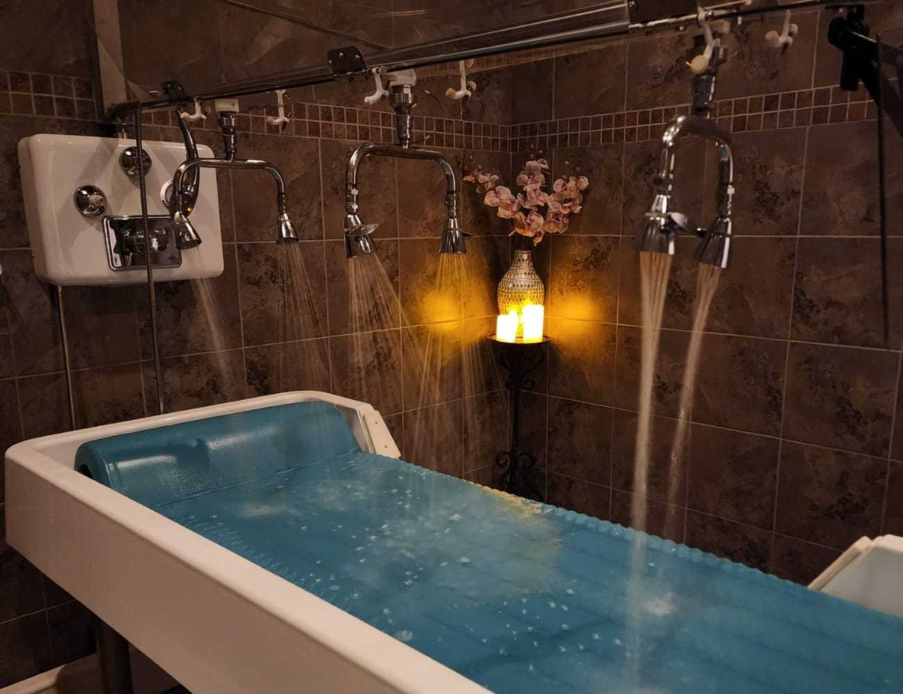 Spa room with multiple showerheads over a treatment table and a glowing candle.