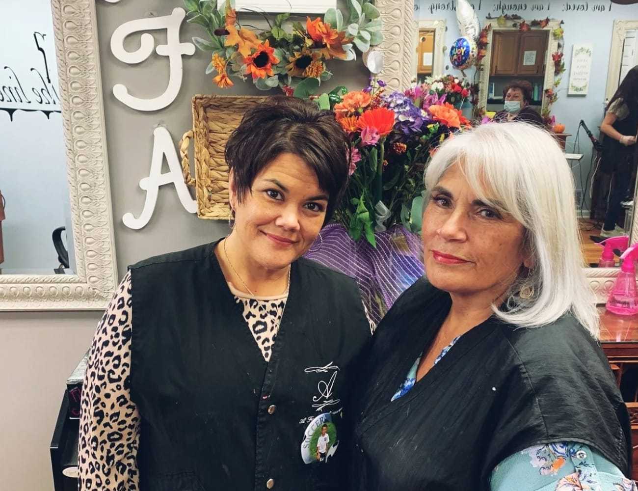 Women smiling in a salon with floral decor and mirror in the background.