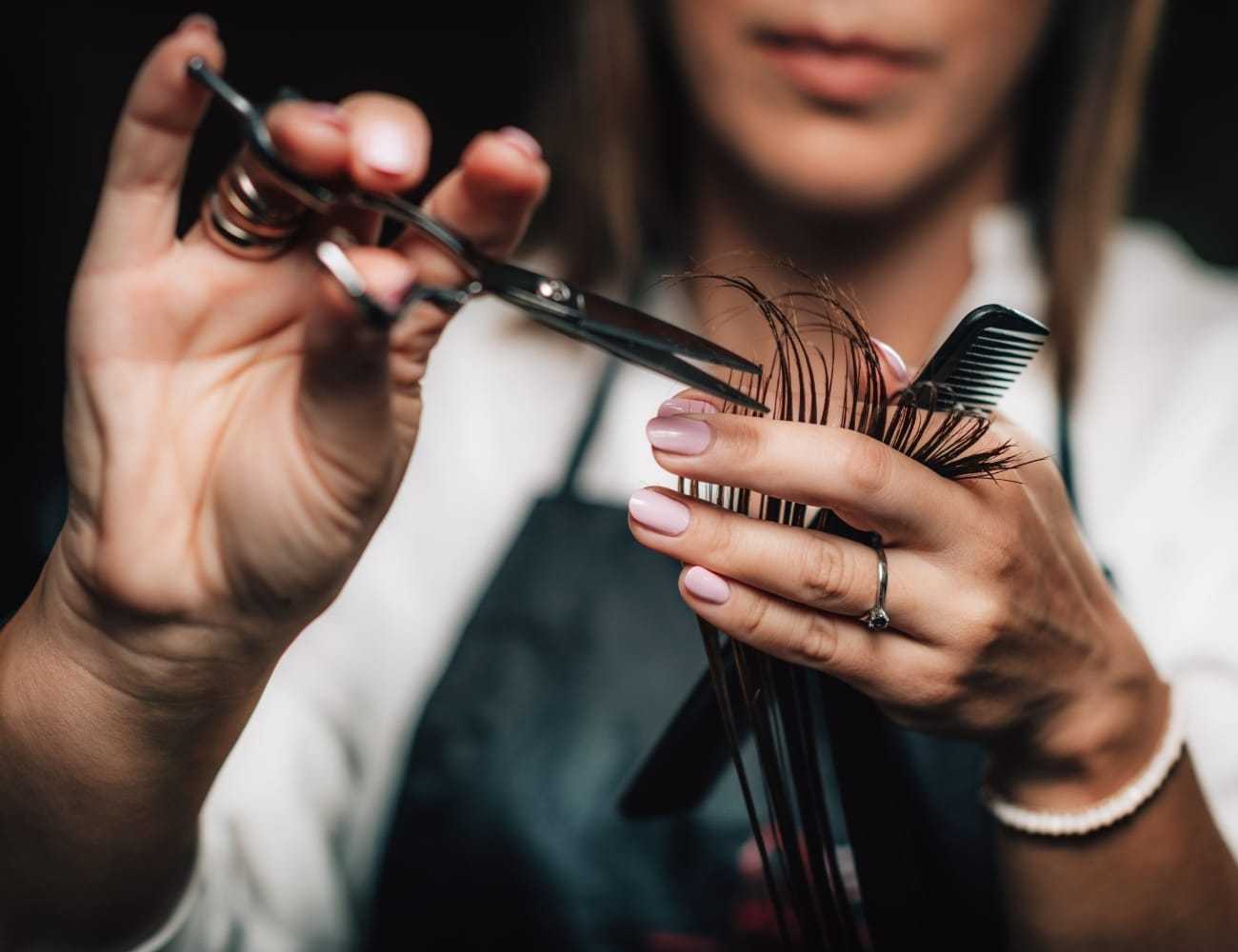 Hairdresser trimming hair with scissors and comb, close-up of hands.