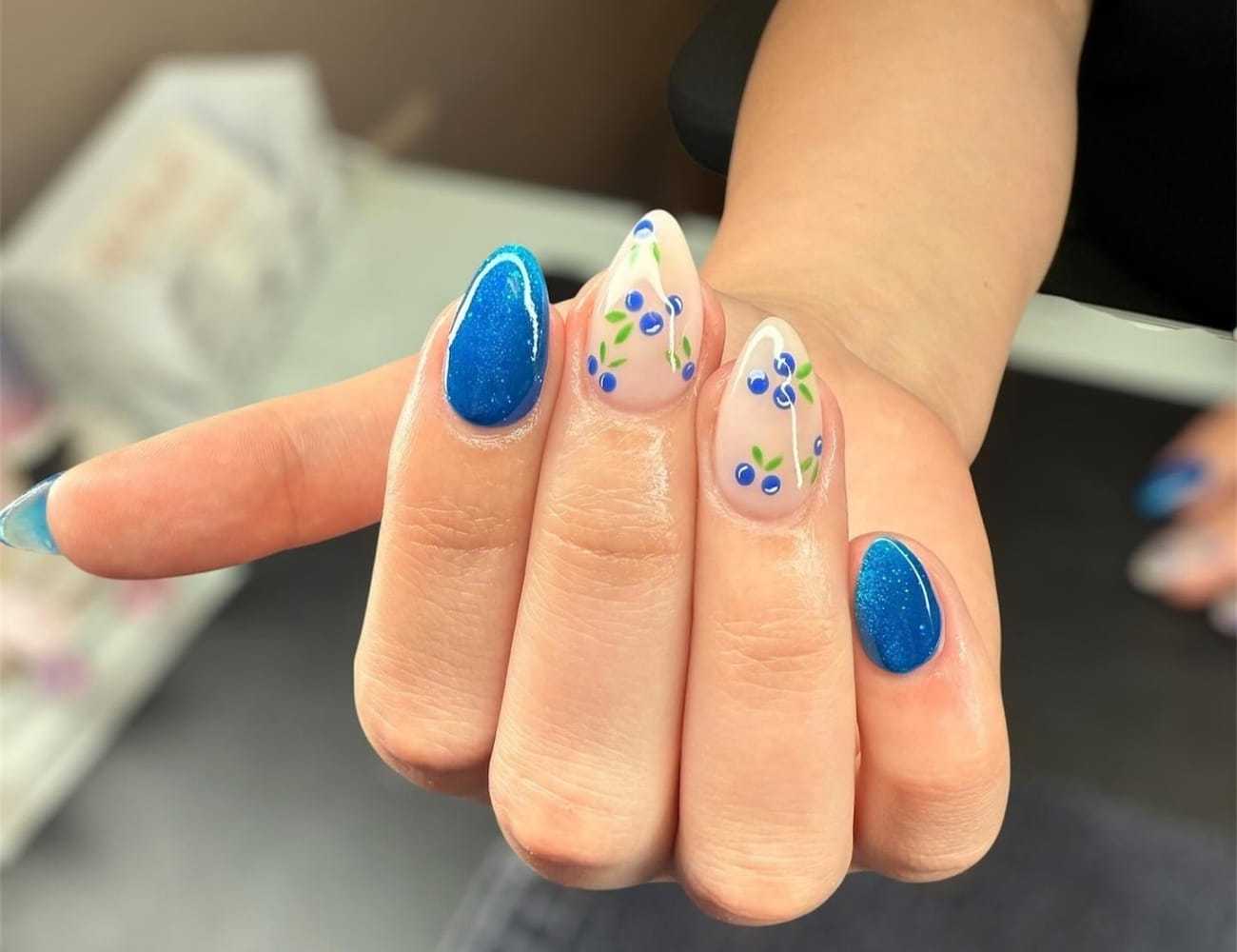 Hand with blue and floral nail art on a light background.
