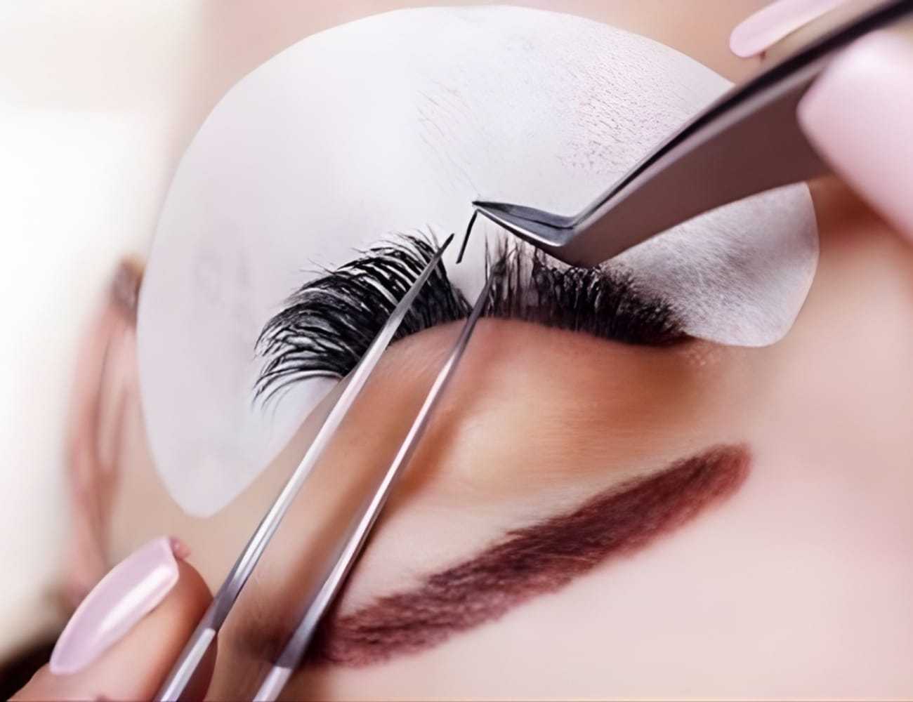 Eyelash extension application with tweezers and protective pad on a client's closed eyelid.
