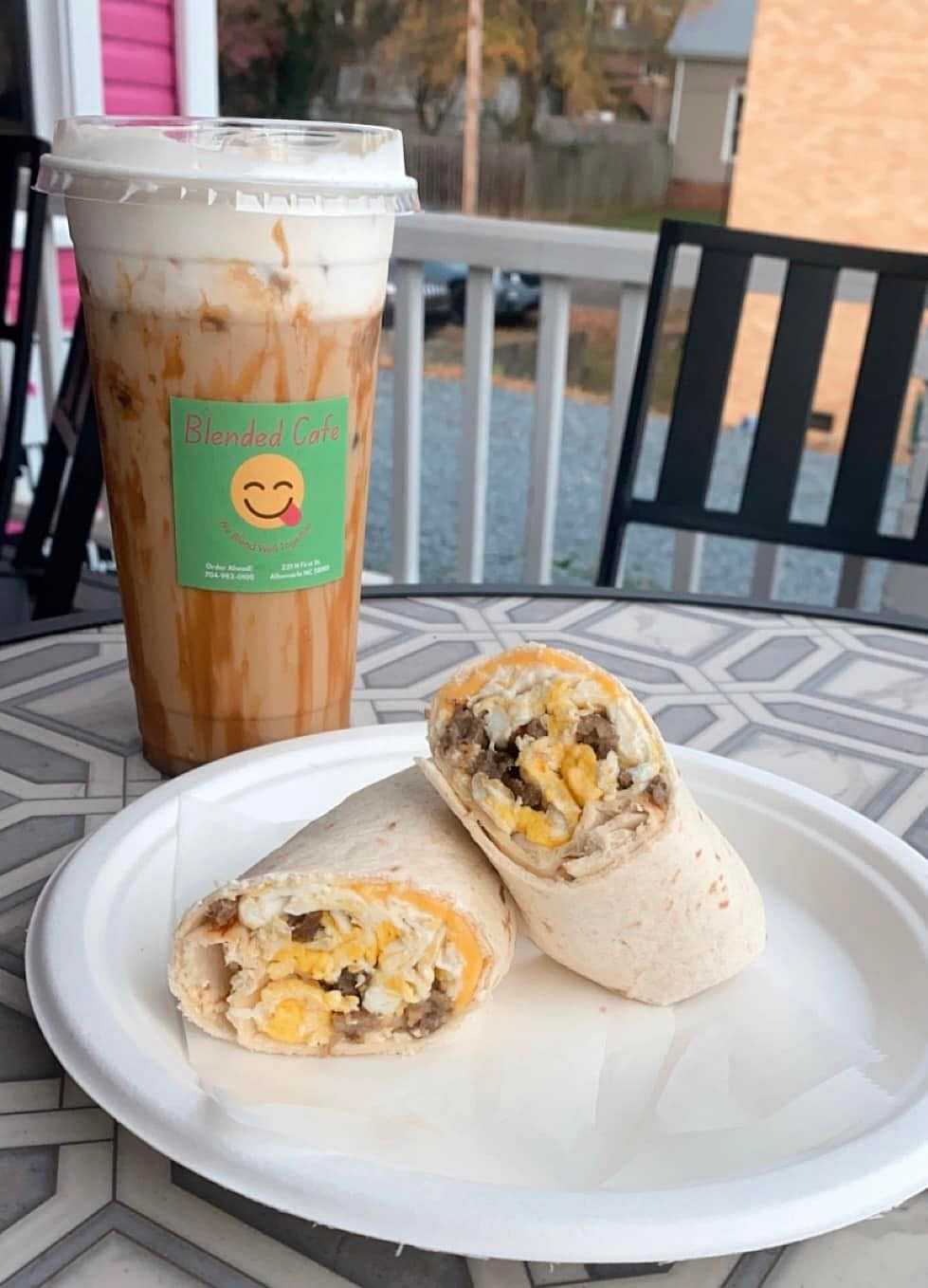 A wrap with scrambled eggs and cheese on a plate, next to a blended coffee from Blended Cafe.