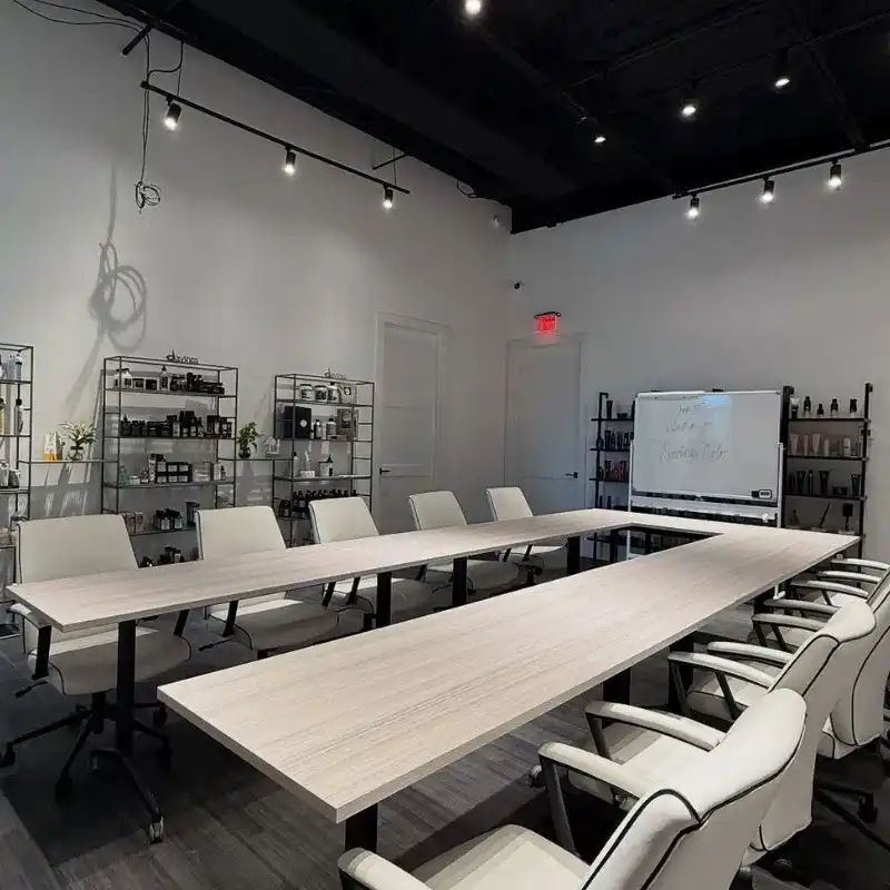 Modern conference room with long tables, white chairs, shelves, and a whiteboard.