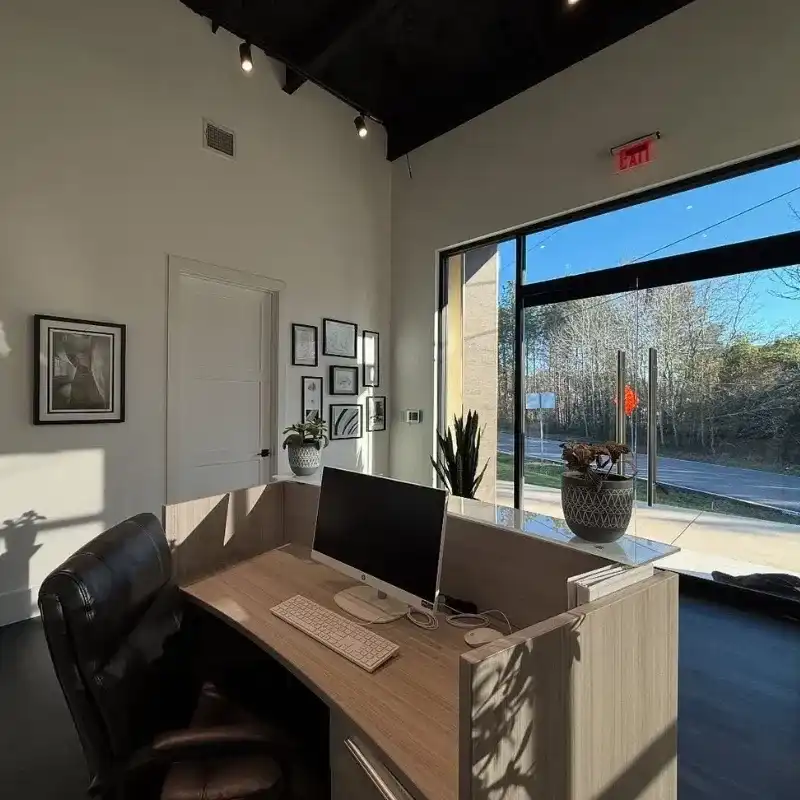 Modern office reception with desk, computer, artwork, and large window.