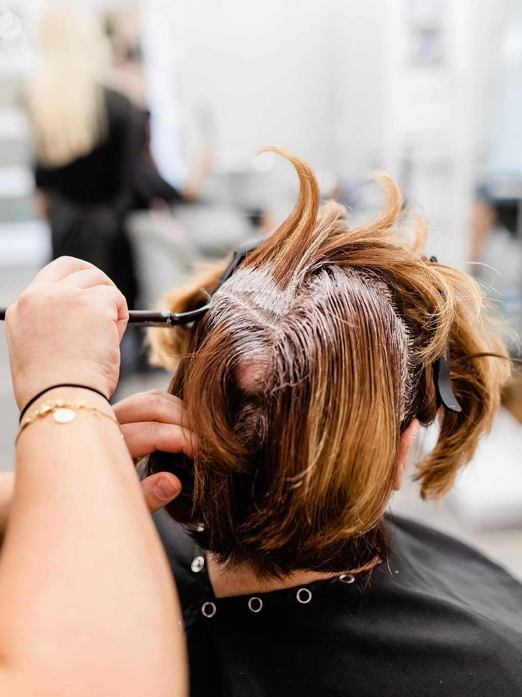 Hairdresser applying color to a client's roots in a salon.