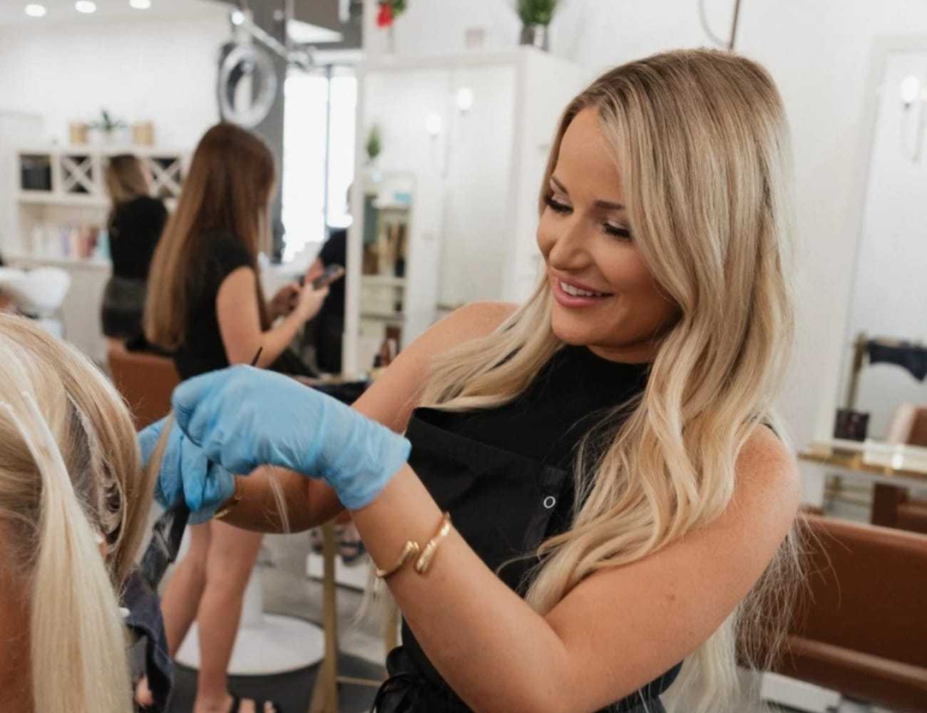 Hairstylist with blonde hair coloring a client's hair in a modern salon.
