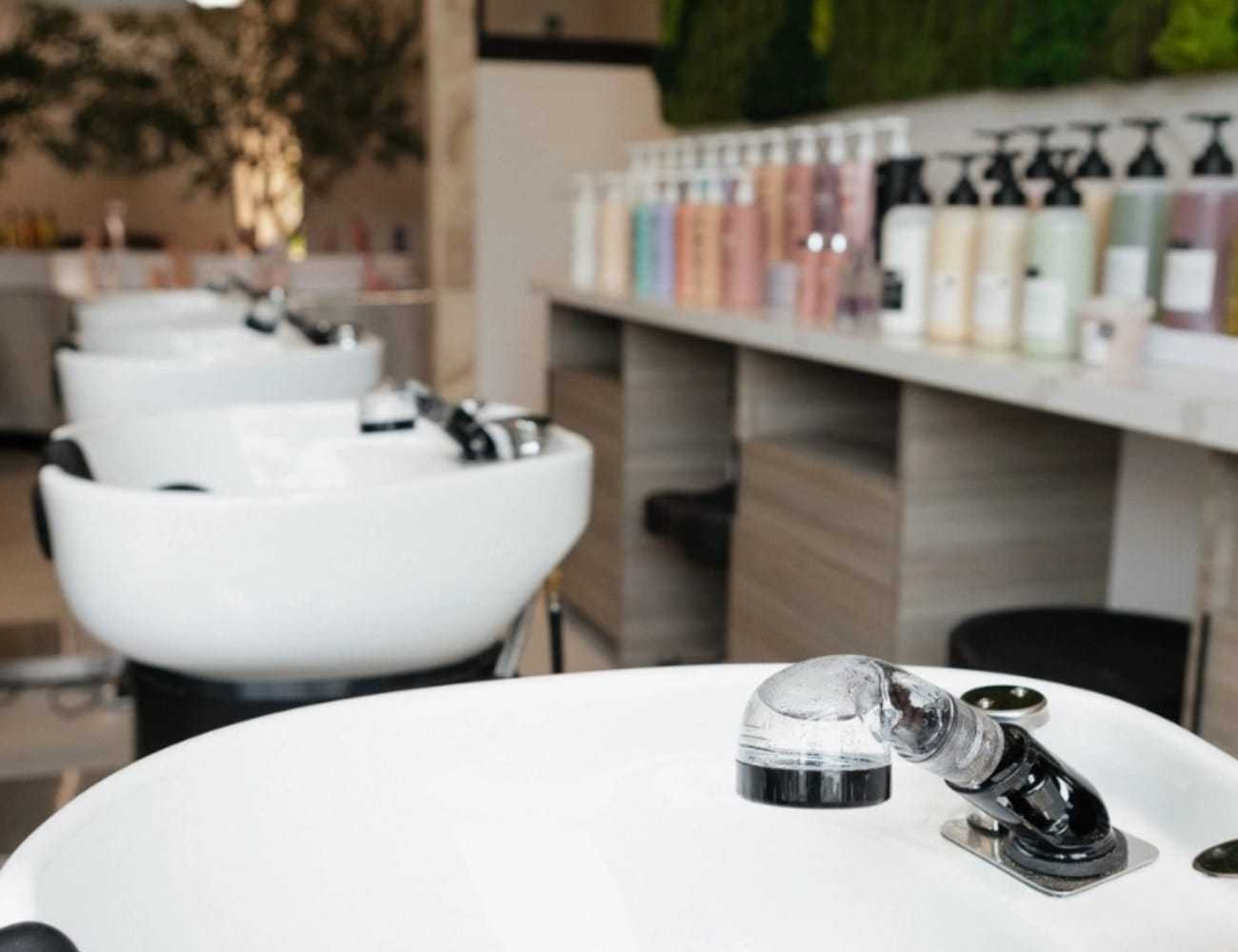Modern salon sinks with various hair products in the background.