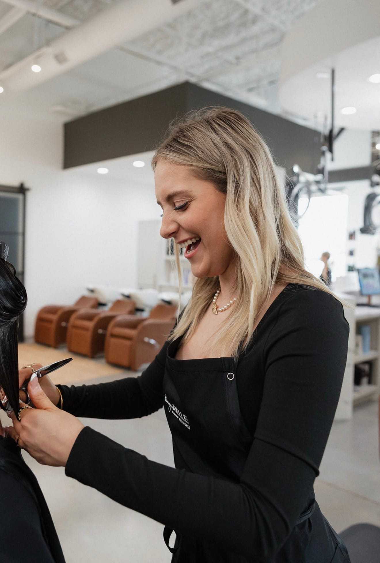 Woman stylist cutting hair in modern salon, smiling while working.