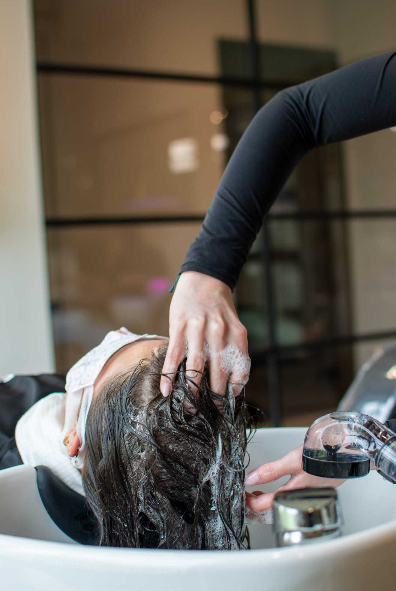 Washing a client's hair at a salon sink while applying shampoo.