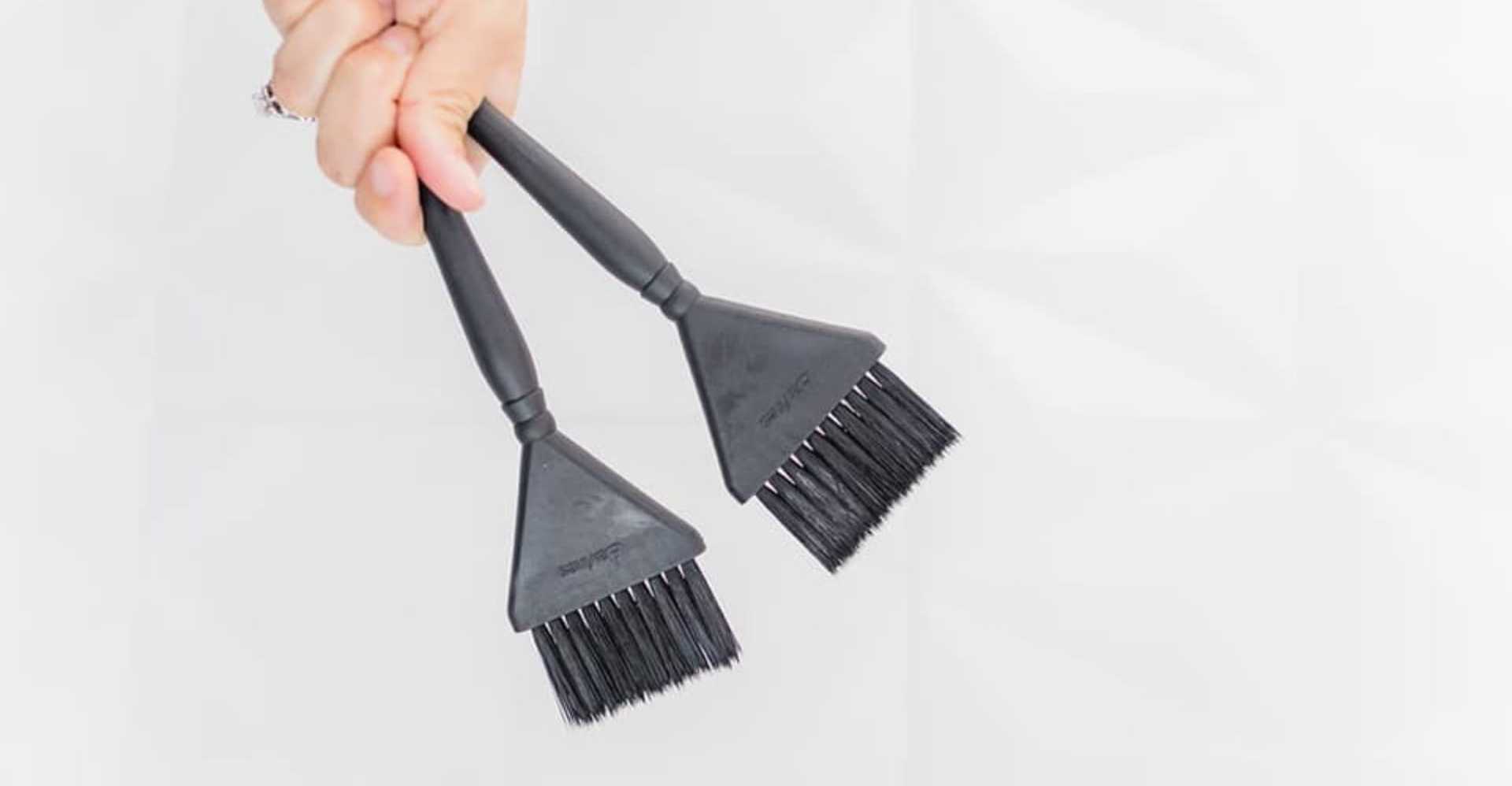 Black plastic grill brushes held in a hand against a white background.