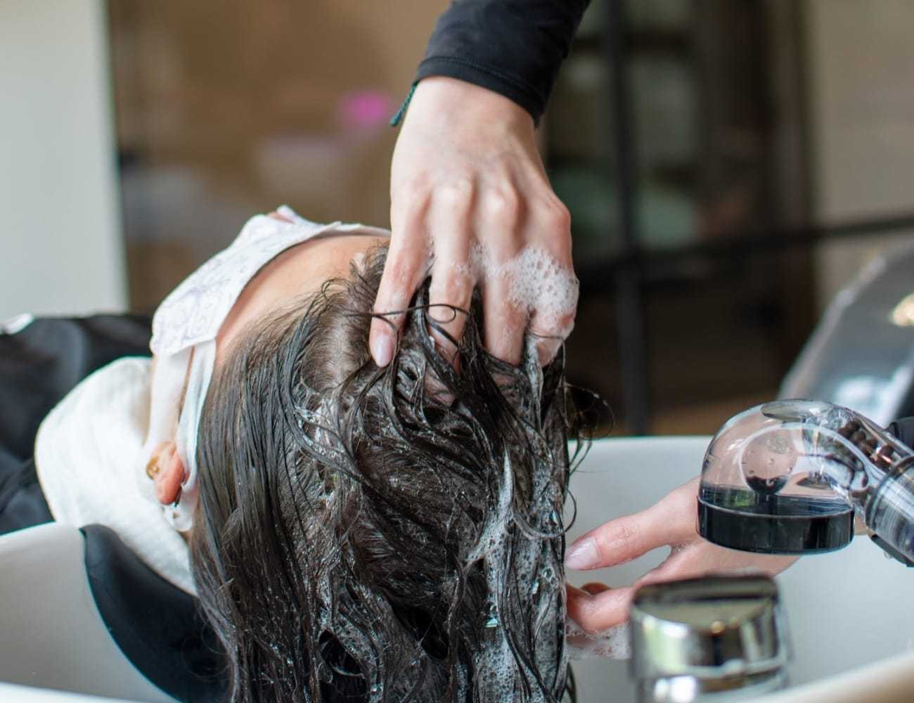 Person having hair washed at a salon sink with hands applying shampoo.