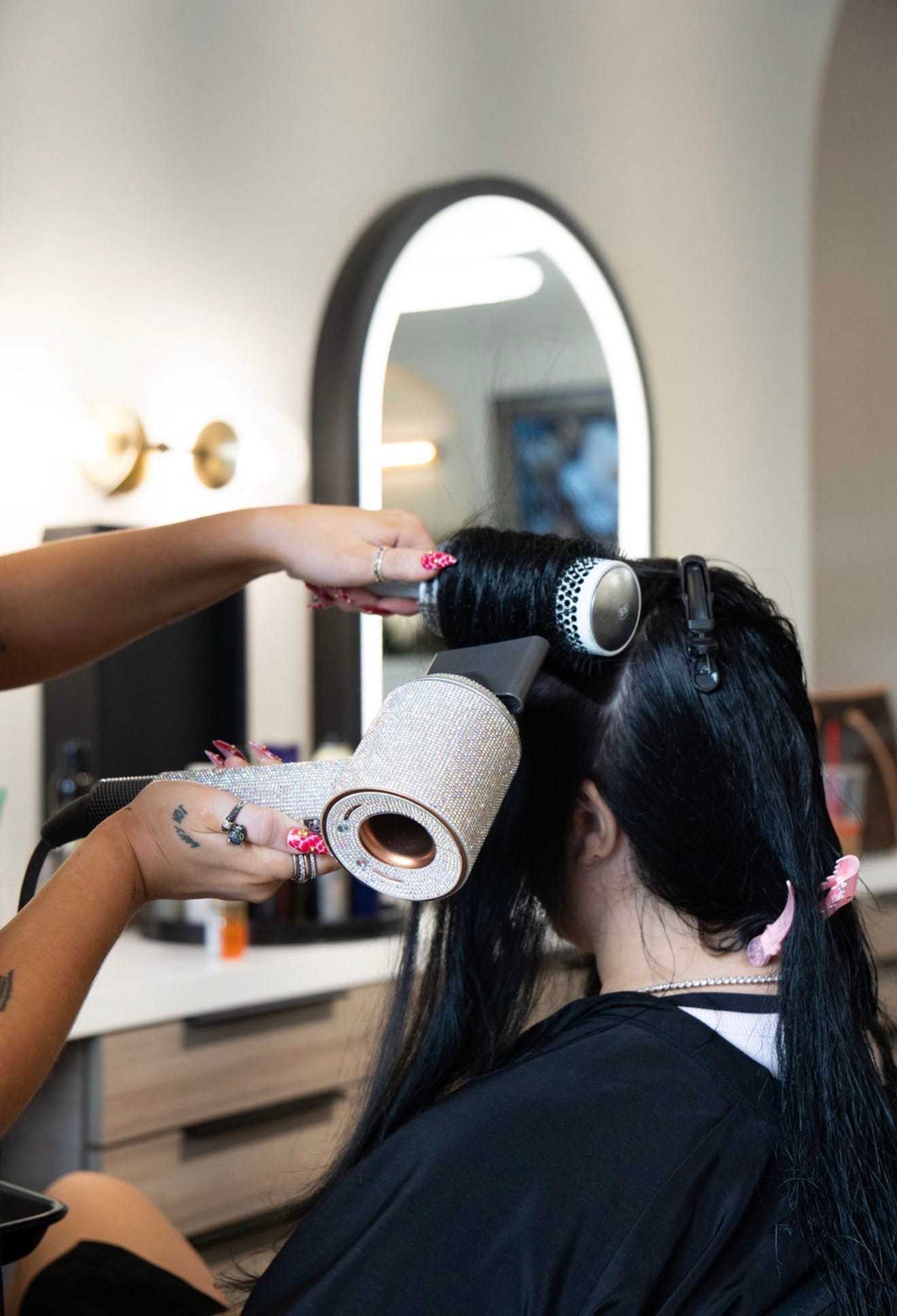 Hair stylist blow-drying and styling a woman's long hair in a salon.