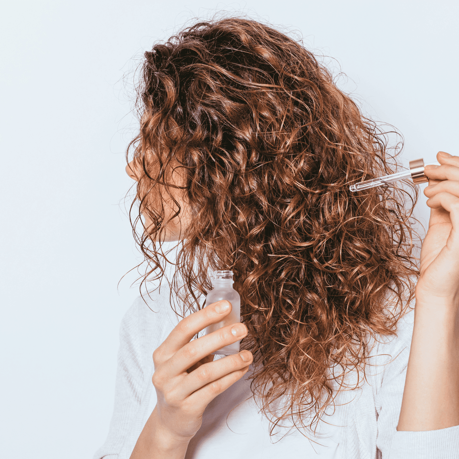 Curly-haired person applying serum with a dropper.