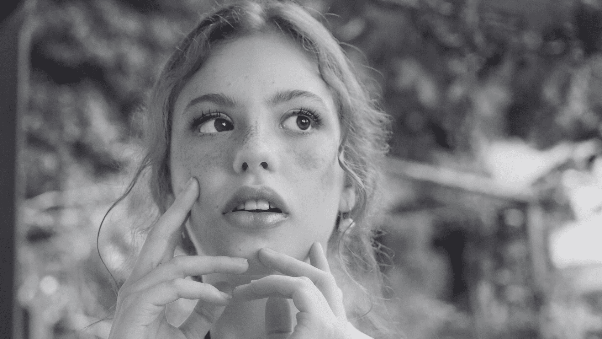Young woman in thought, gazing upwards in a natural outdoor setting, black and white.