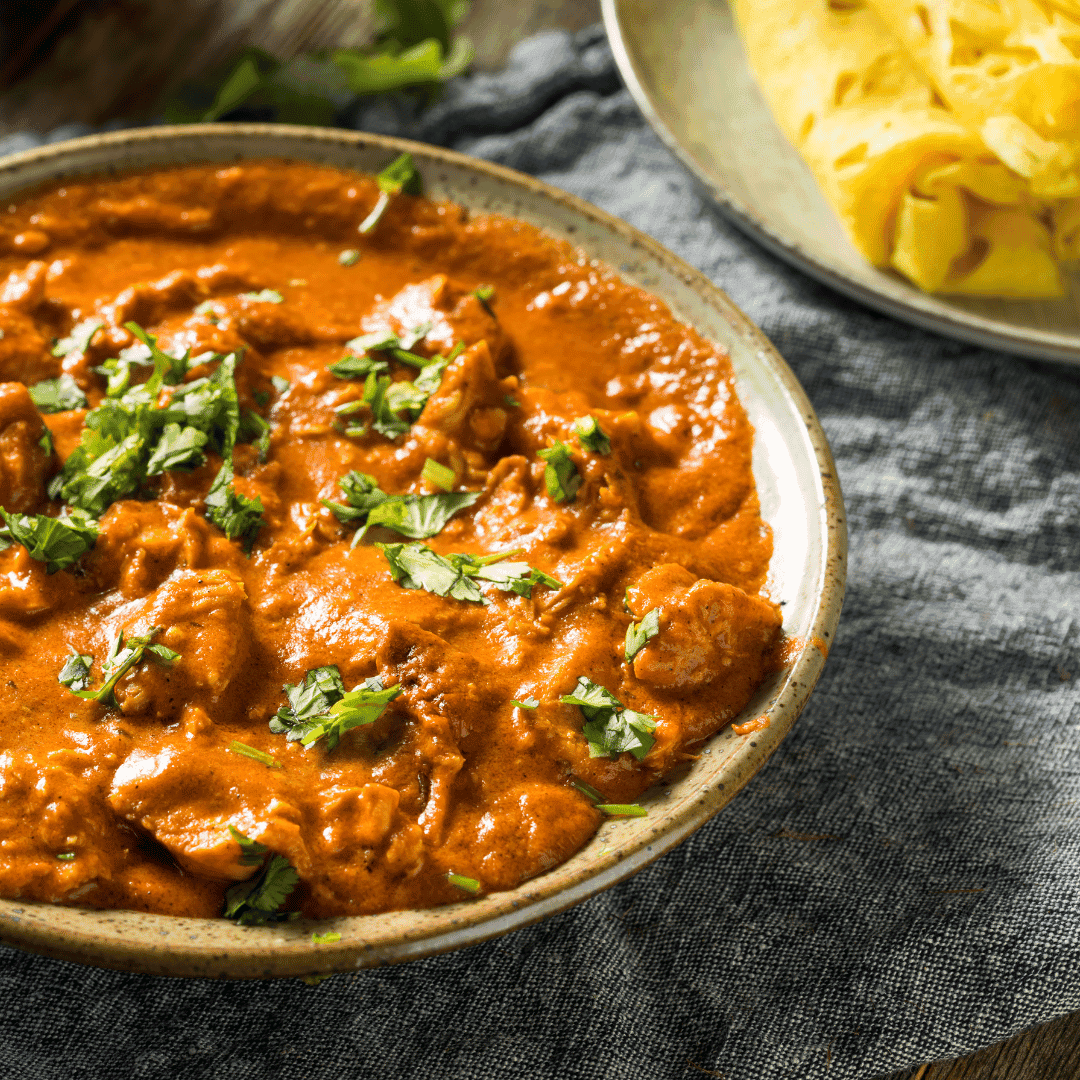 Bowl of creamy chicken tikka masala garnished with cilantro, served with Indian bread.