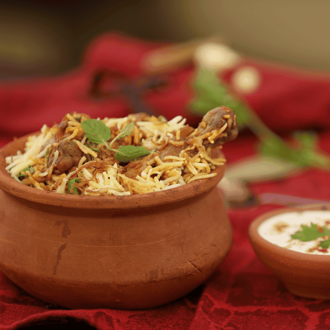 Clay pot filled with flavorful biryani garnished with herbs, placed on a red cloth with yogurt.