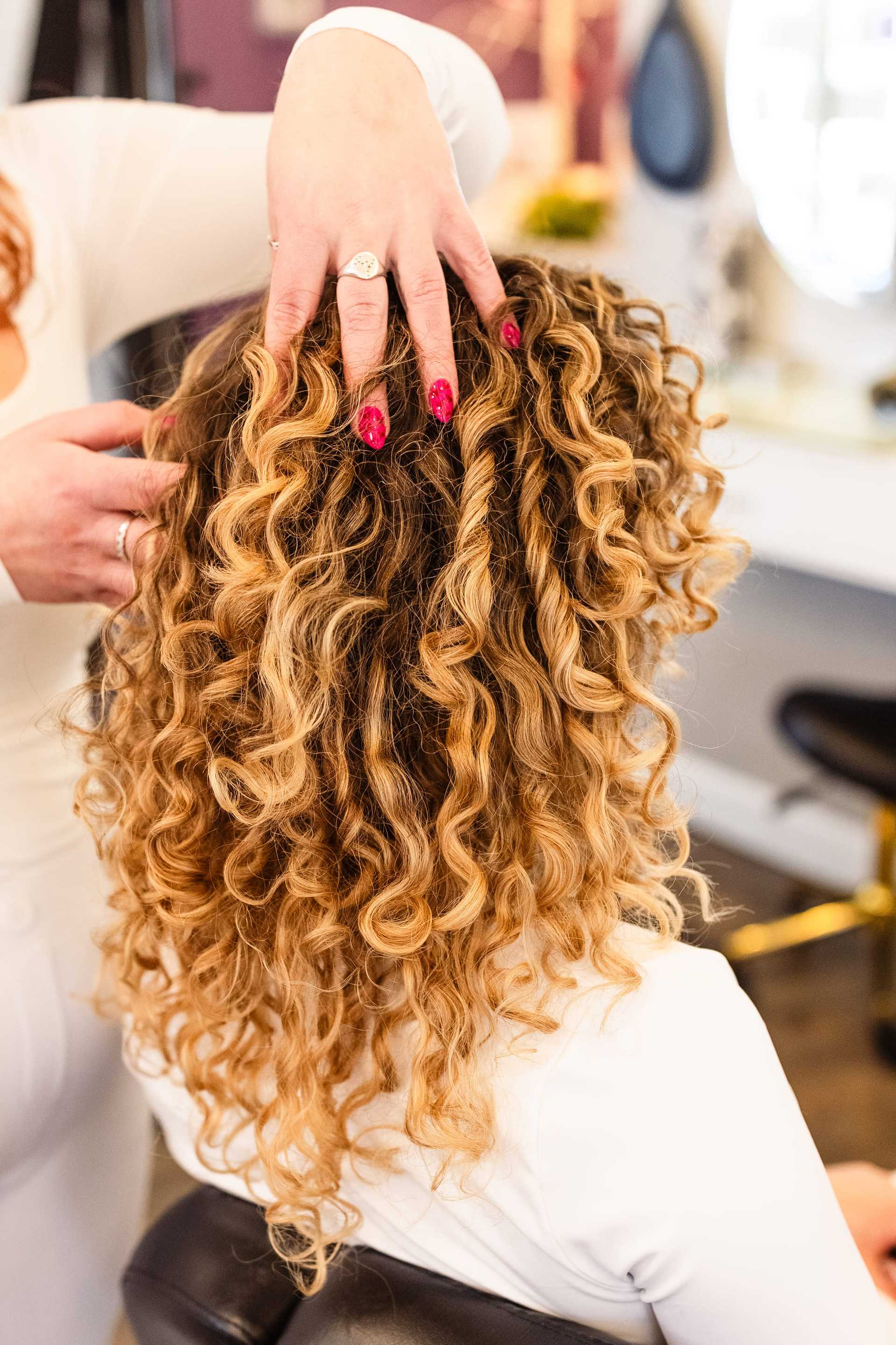 Hair stylist arranging client's blonde curly hair in salon.