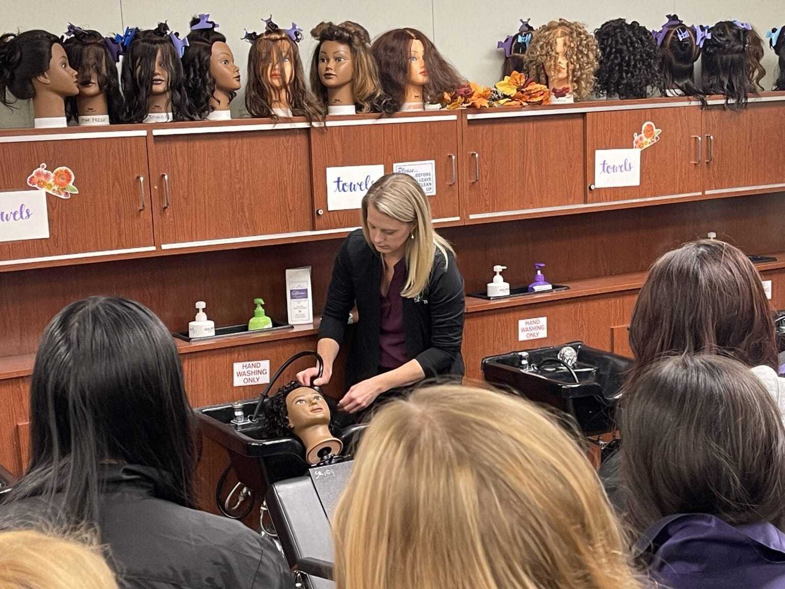 Hairdressing class demonstrating styling techniques on mannequin heads.