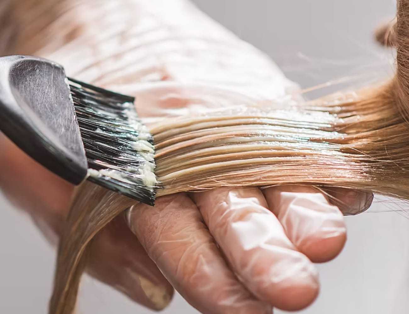 Hair being dyed with a brush and gloves in a salon setting.