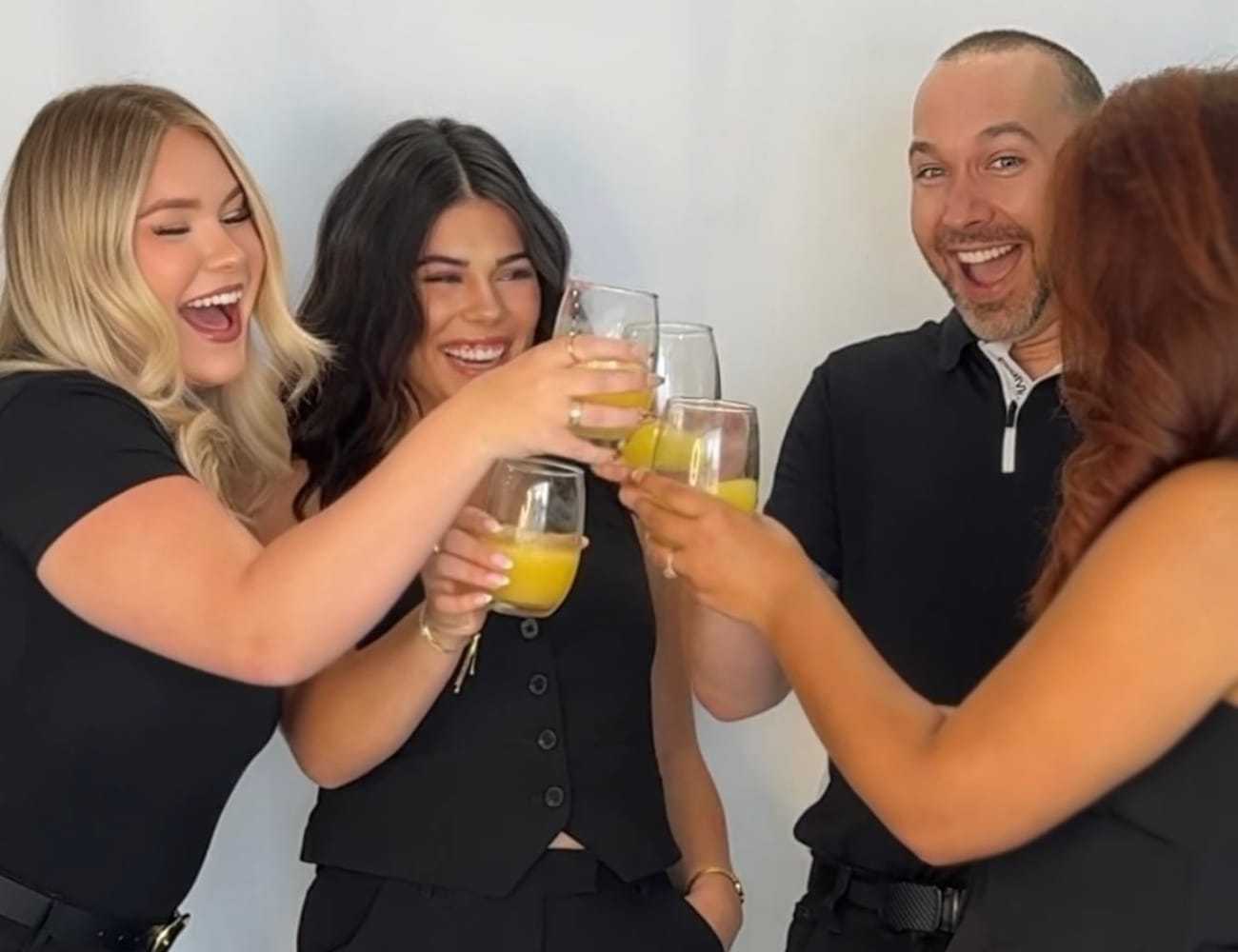Group of people joyfully toasting with drinks, dressed in black attire.