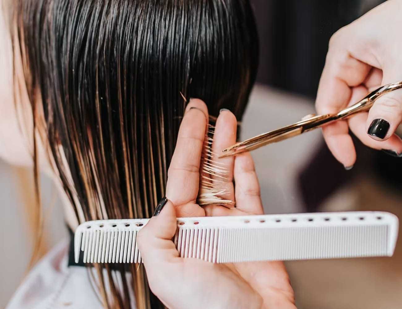 Hair being trimmed with scissors and comb in a salon setting.
