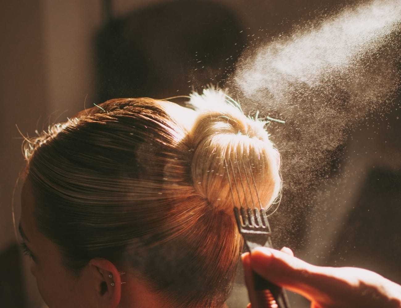 Hair stylist applying spray to a woman's styled bun.