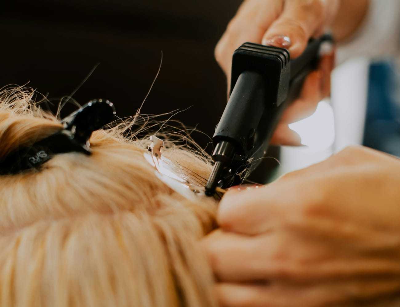 Hair extensions being applied using a hot tool in a salon.