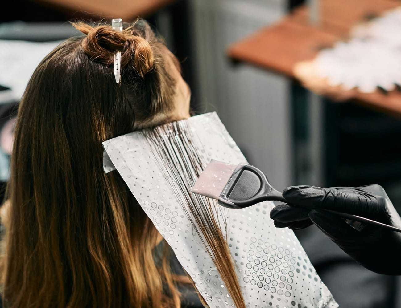 Hairdresser applying dye with brush to woman's hair in salon.