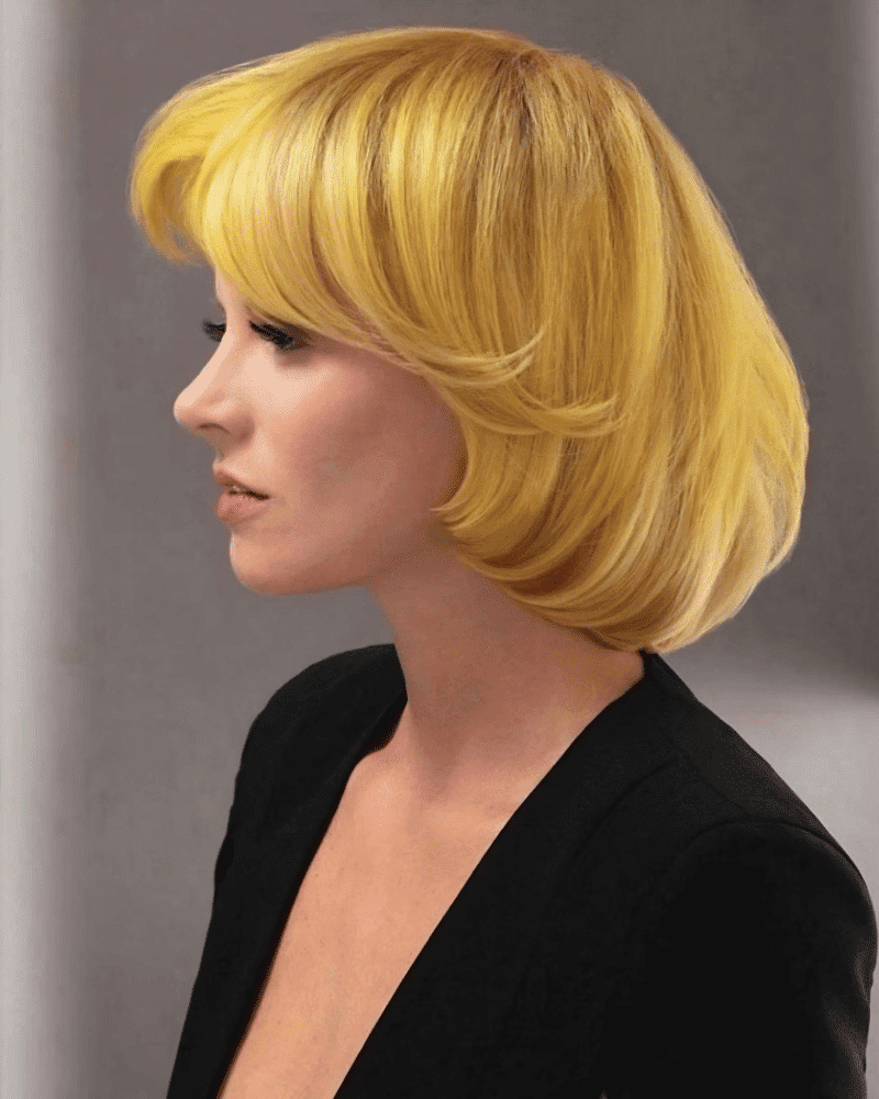 A woman with short blonde hair in profile, wearing a black outfit against a muted backdrop.