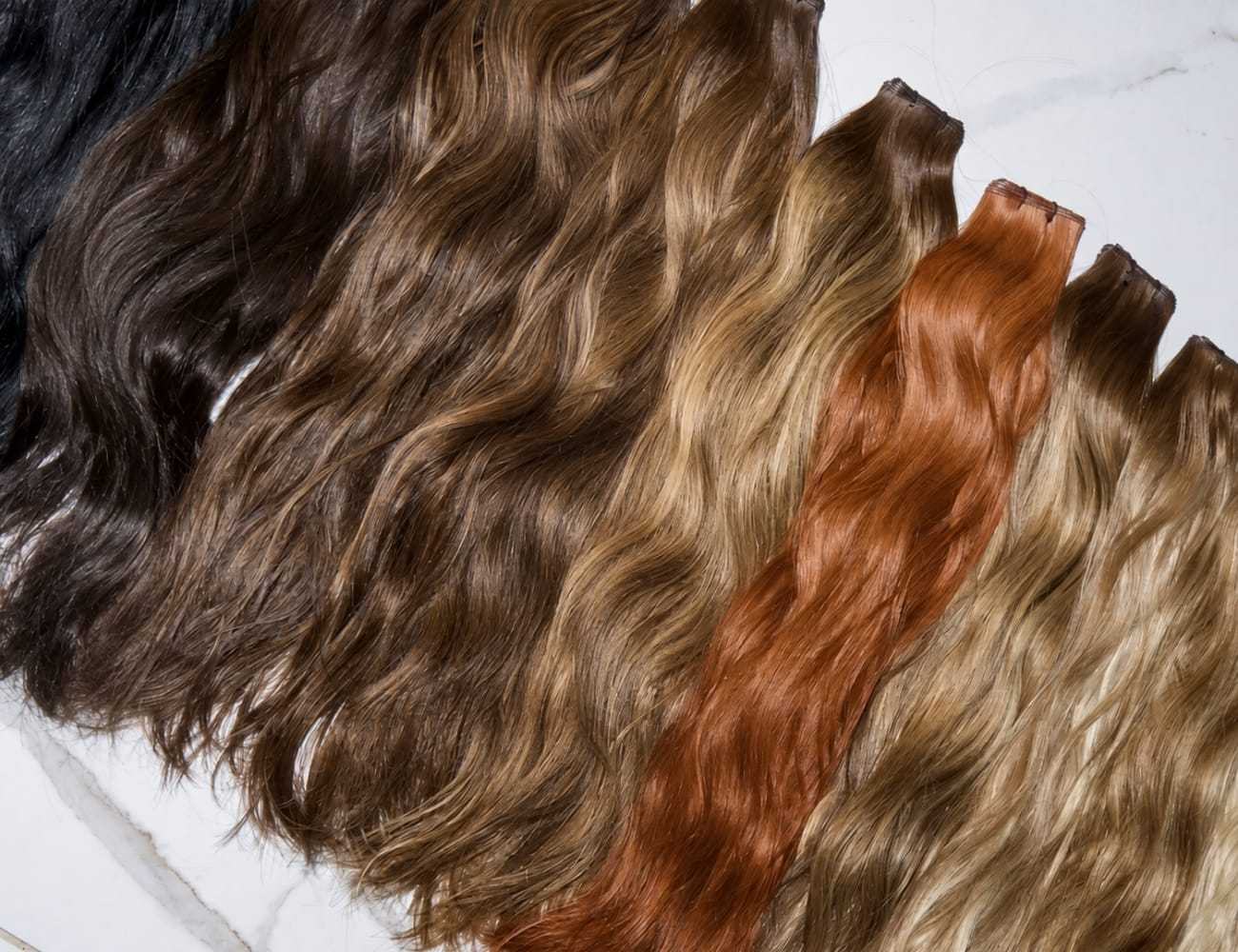 Various shades of wavy hair extensions displayed on a white surface.