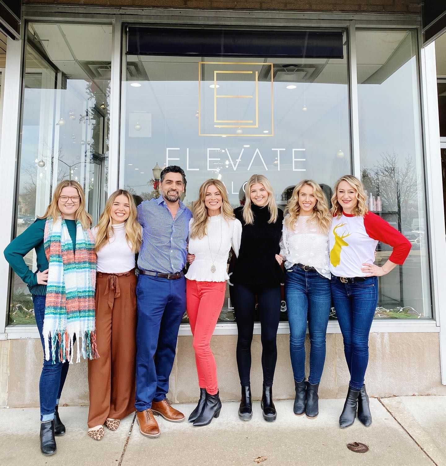 Group of smiling people standing in front of Elevate Salon storefront.
