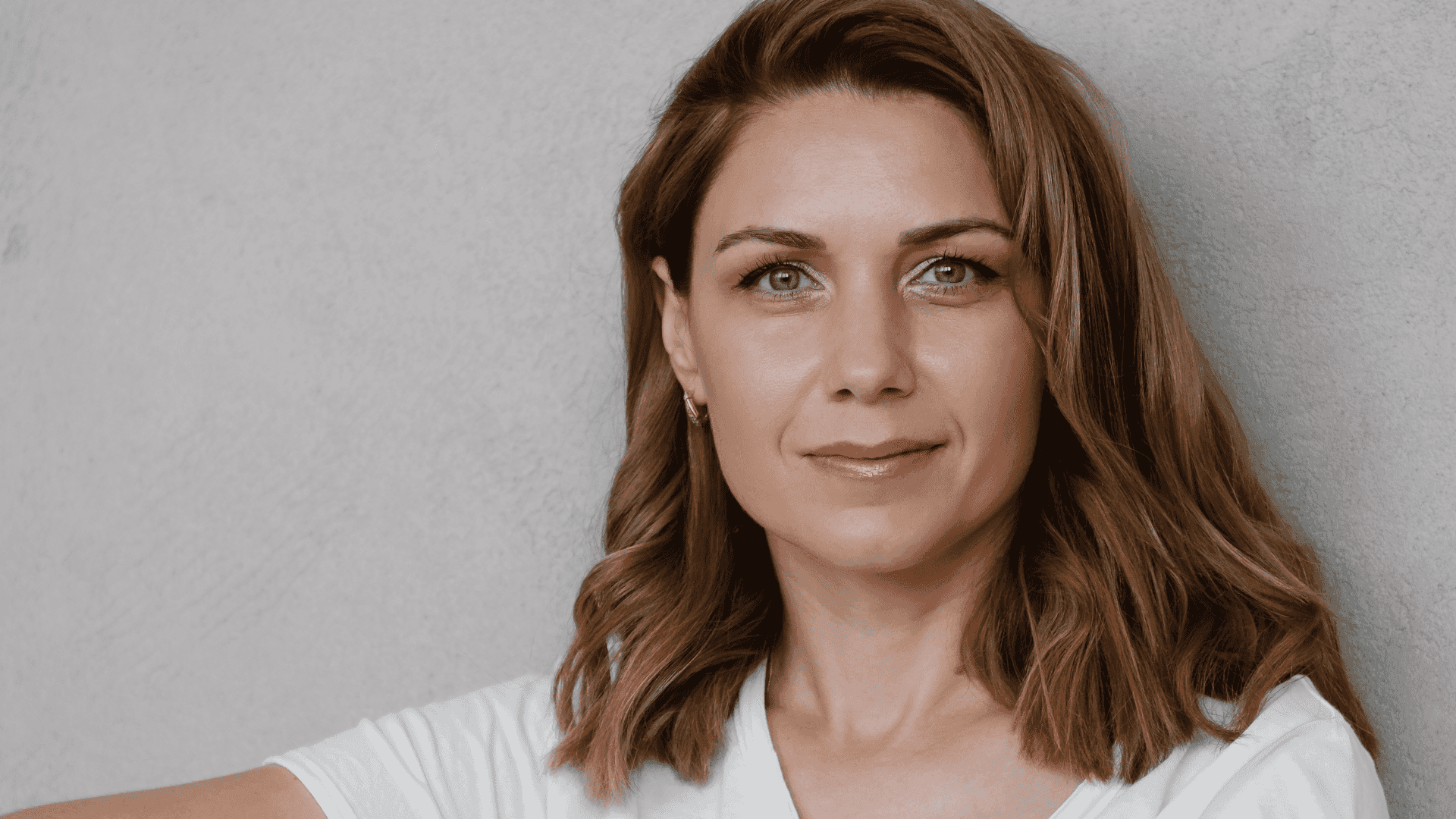 Woman with medium-length brown hair and a neutral expression, wearing a white top.