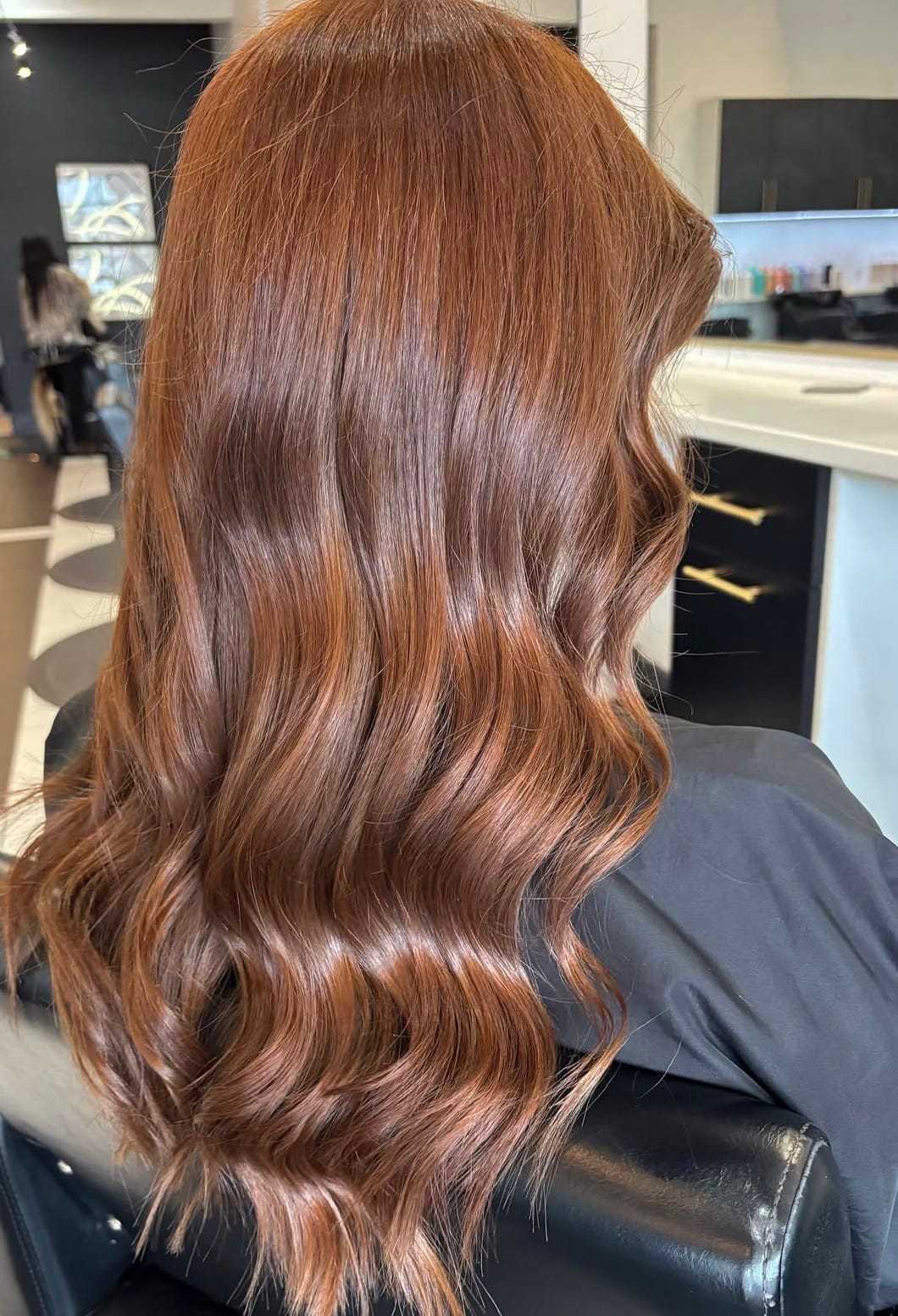Wavy, shiny, auburn hair on a person seated in a modern salon.