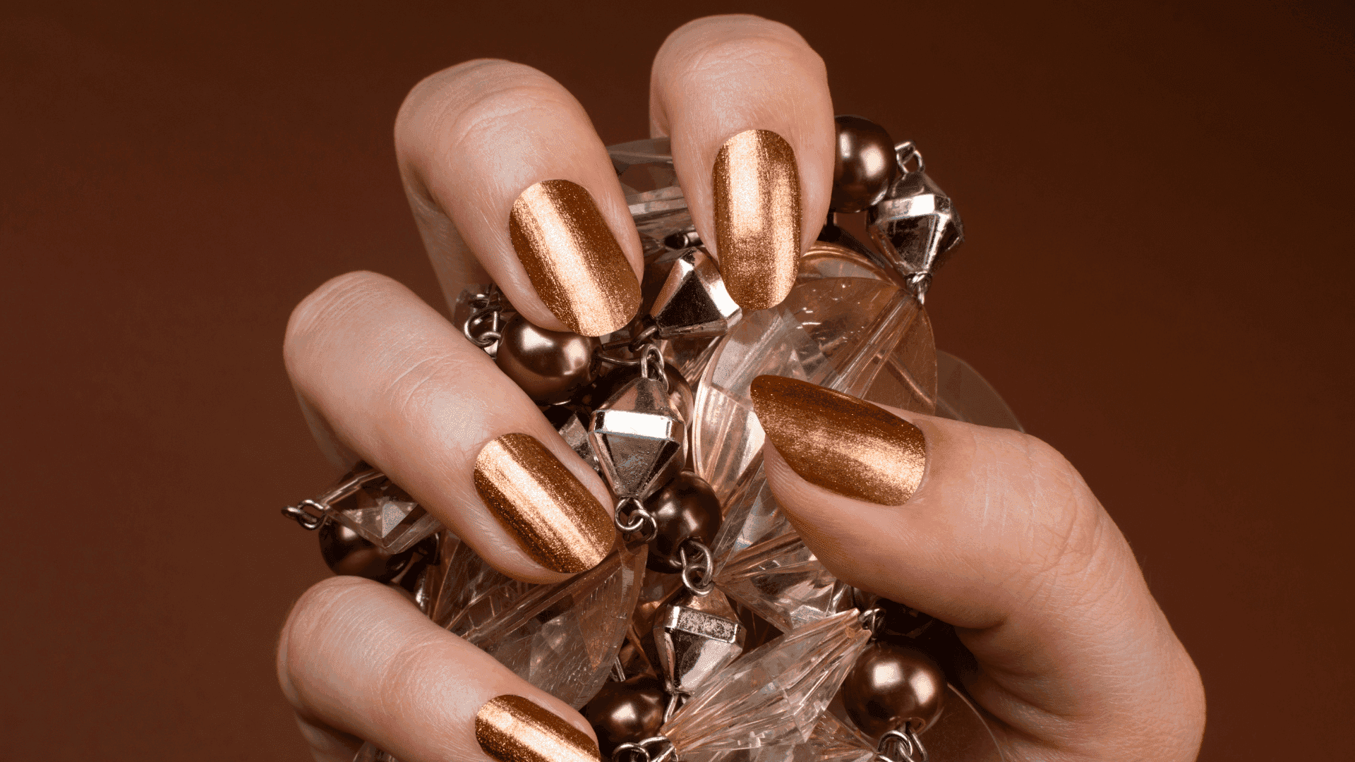 Shiny bronze manicured nails holding a crystal-accented bracelet.