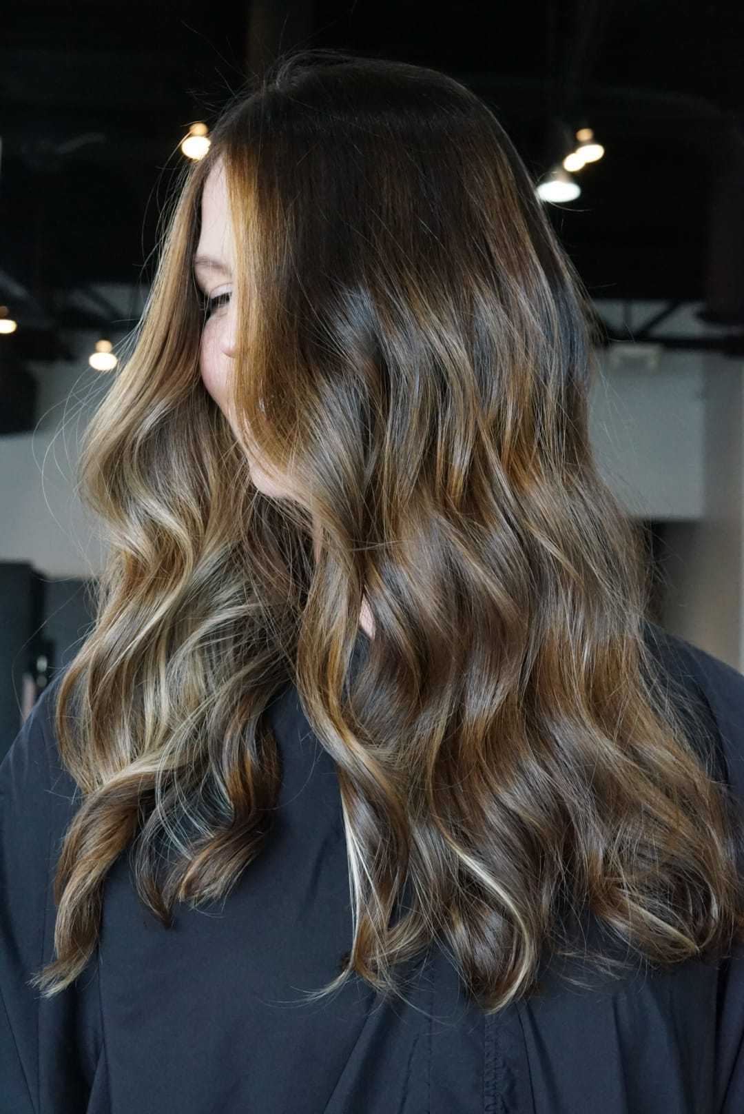 Long, wavy brunette hair with highlights, styled in a salon setting.