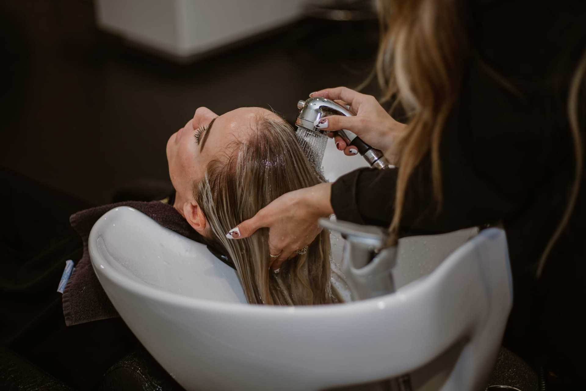 Hairdresser washing a client's hair in a salon sink.