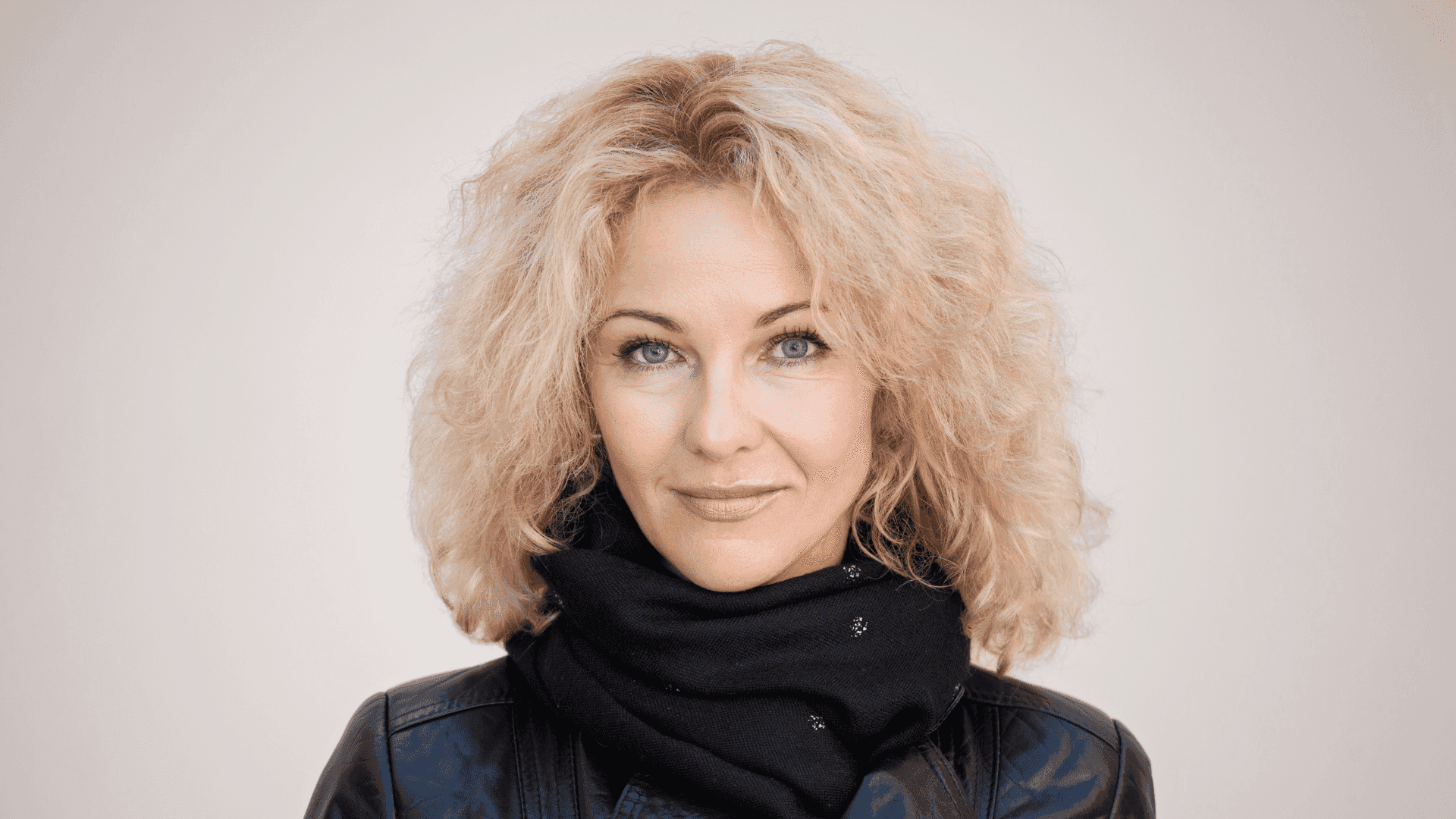 Portrait of a woman with curly blonde hair, wearing a black leather jacket and scarf.