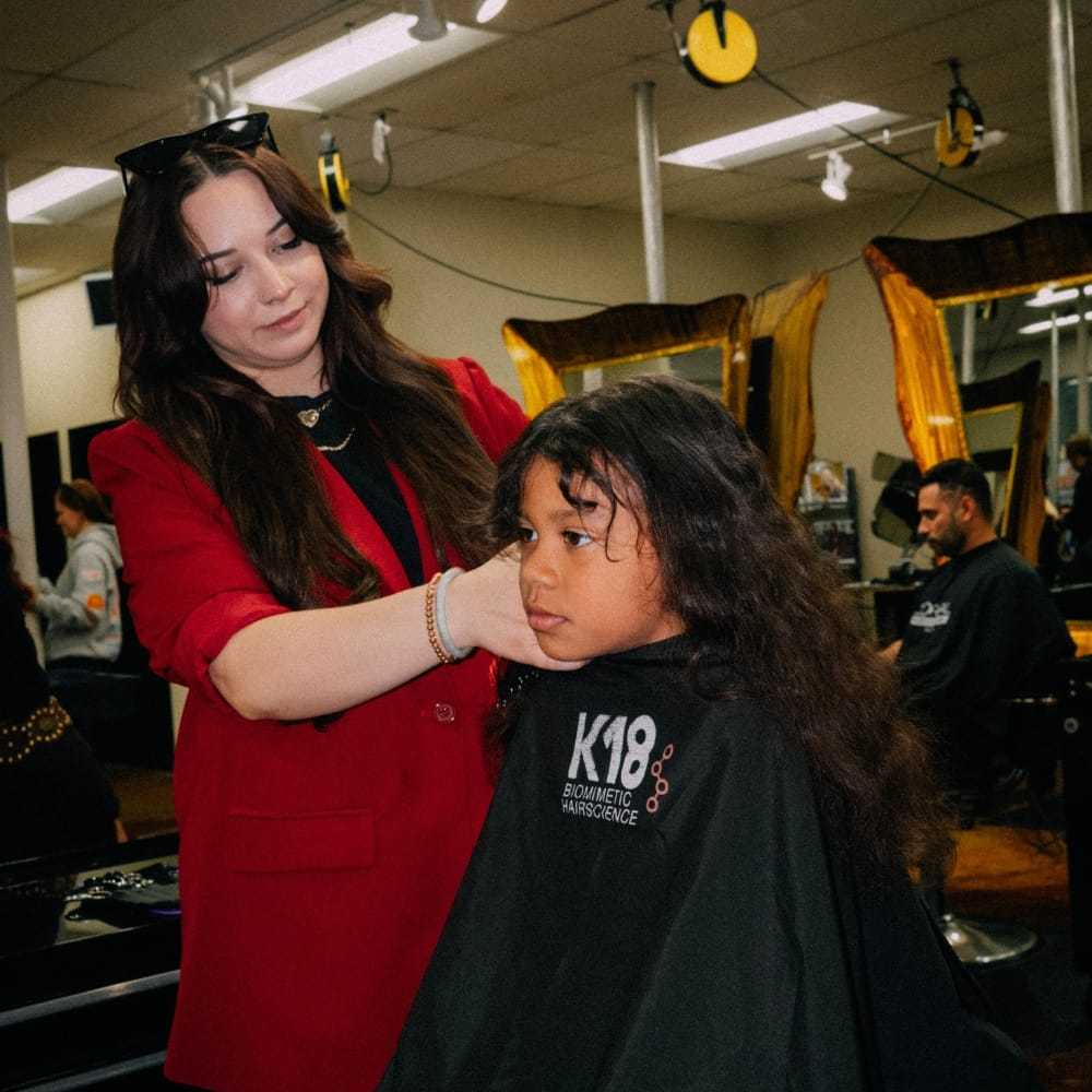 Stylist cutting a child's long hair at a salon.