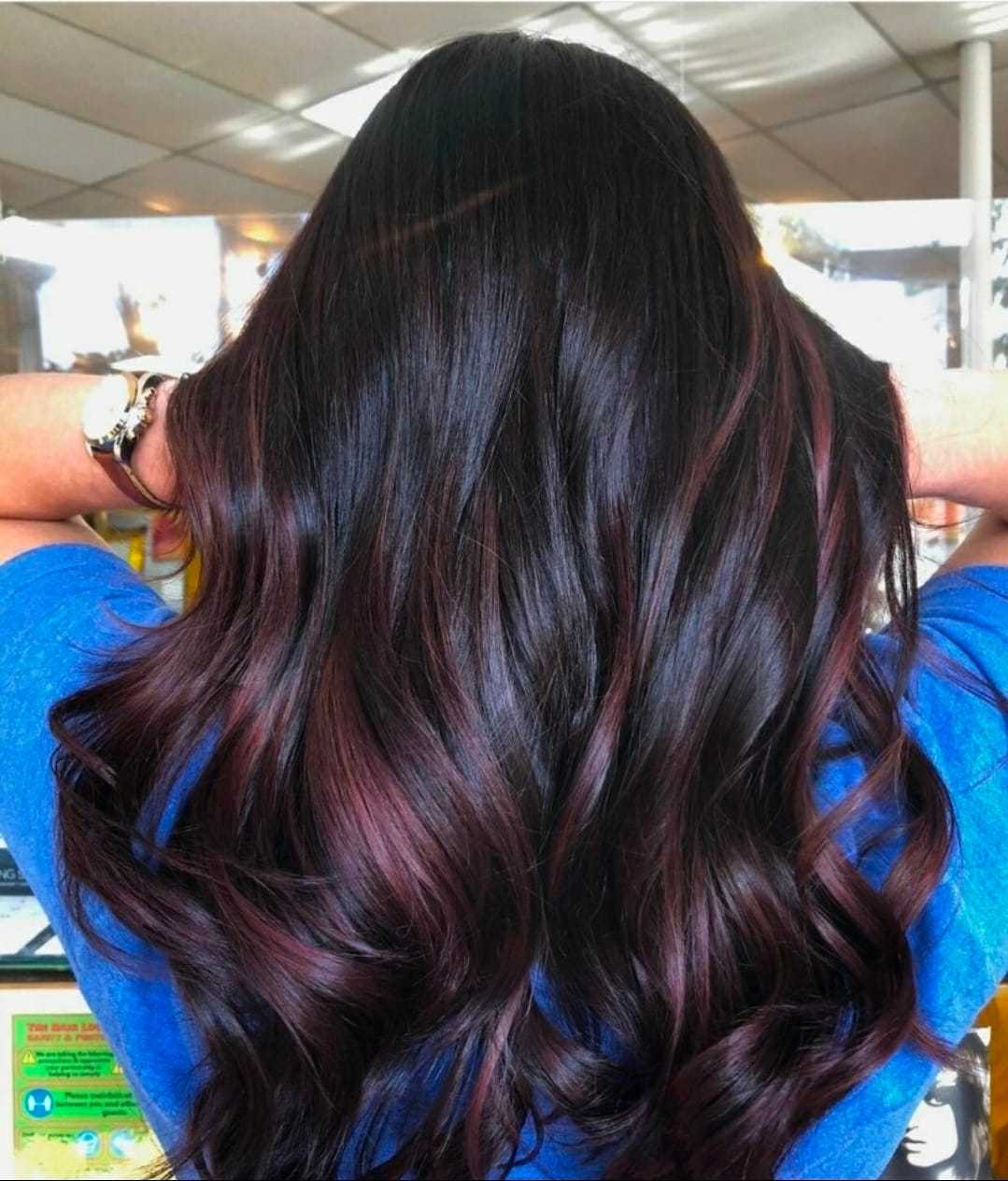 Long, wavy hair with dark and red tones in a bright salon setting.