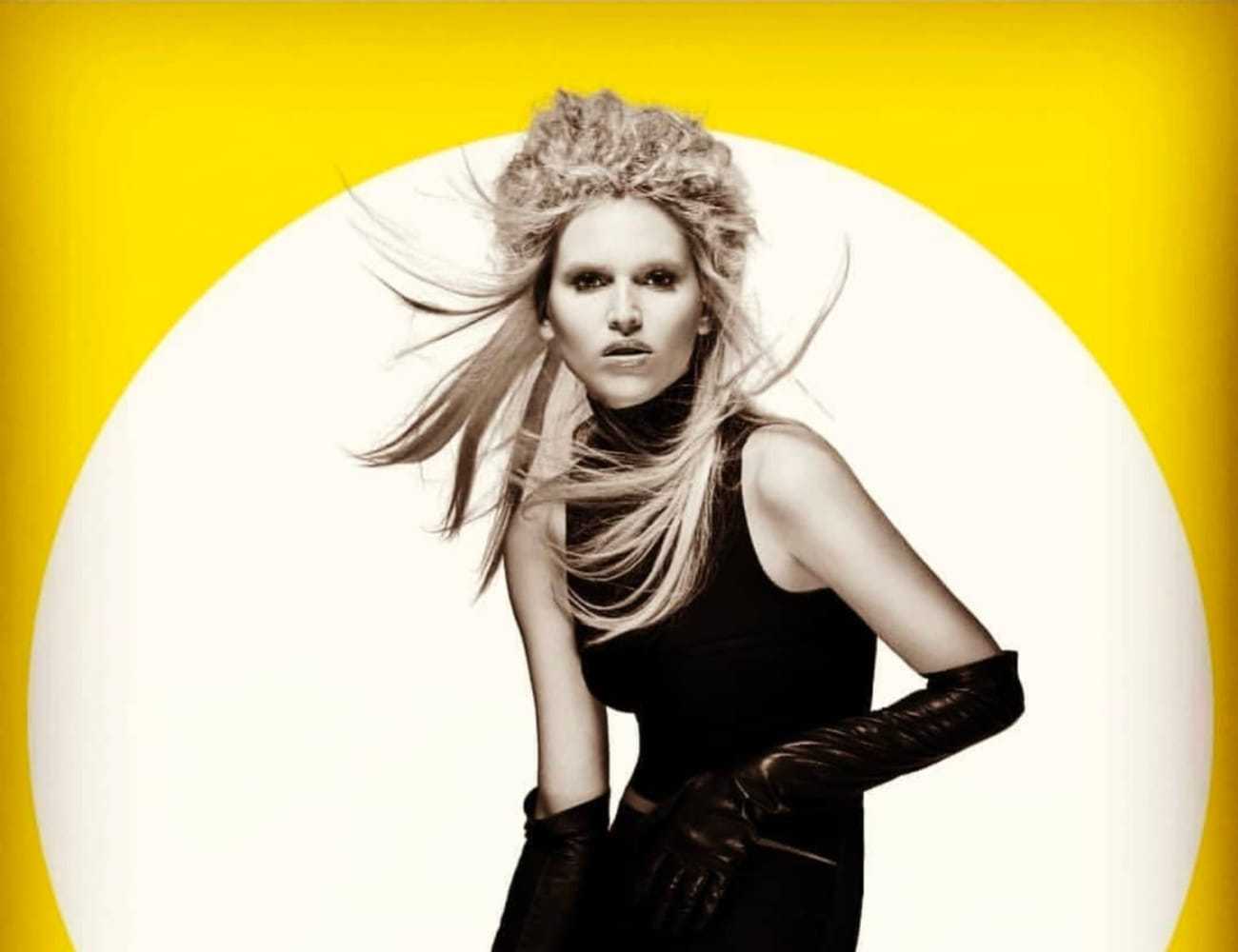 A woman with striking hair poses in front of a bright yellow and white background.