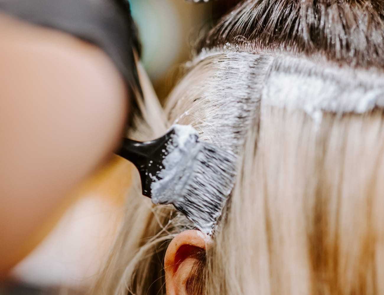 Hair stylist applying dye to client's roots with a brush in a salon.